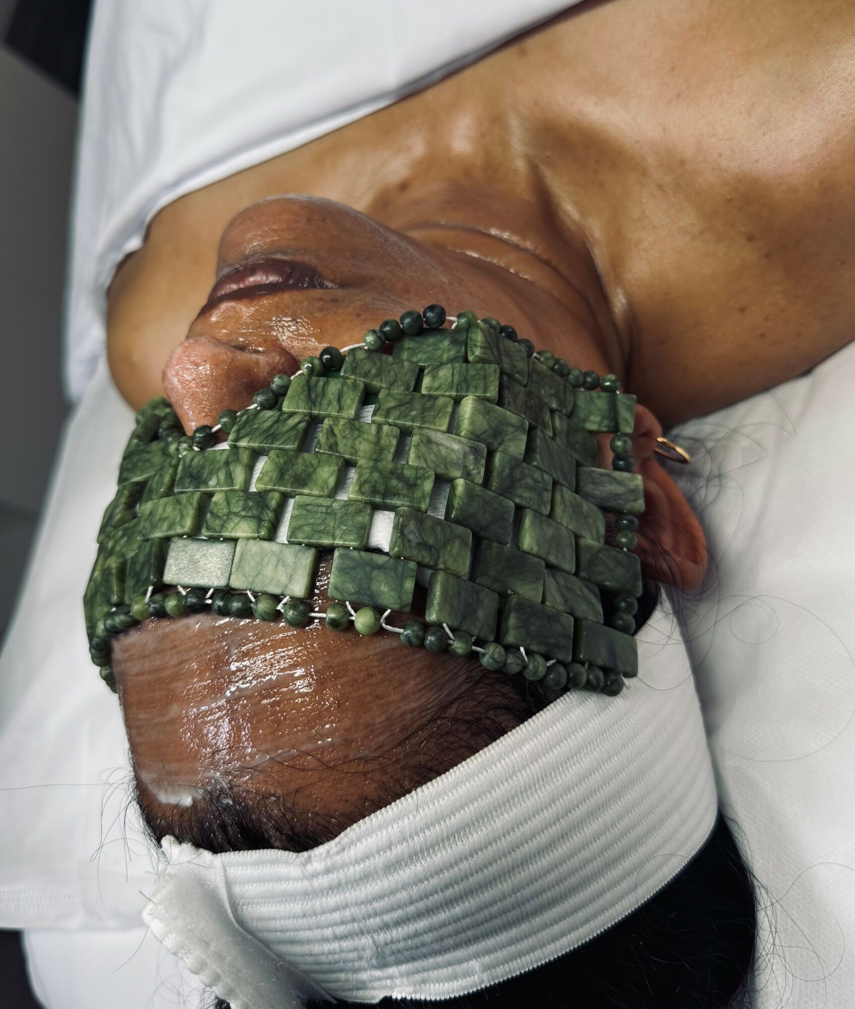 Person lying down with head wrapped in a white cloth, face partially covered with green woven material, skin visible.