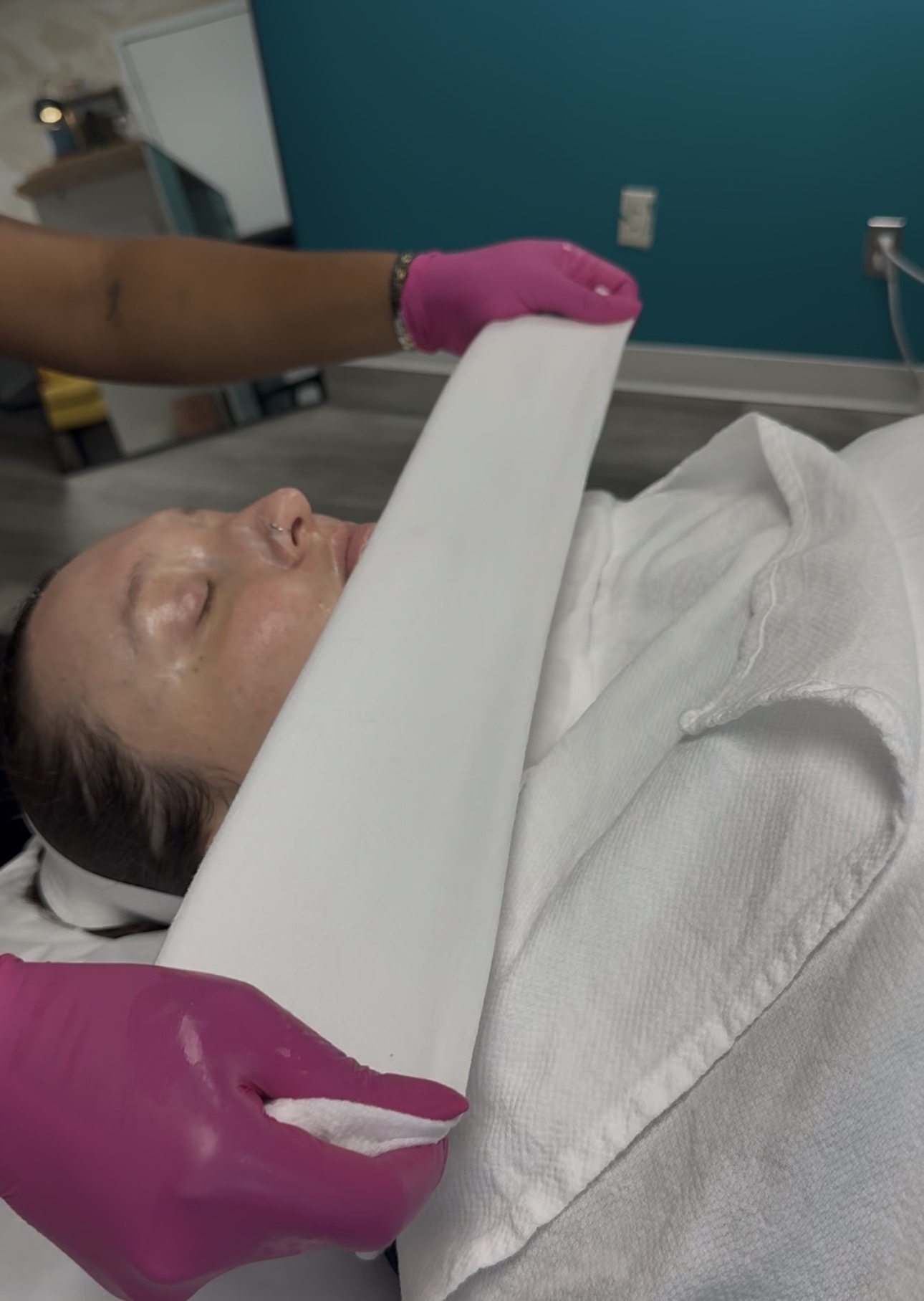 Person lying in hospital bed with a white board being held by a healthcare worker wearing pink gloves.