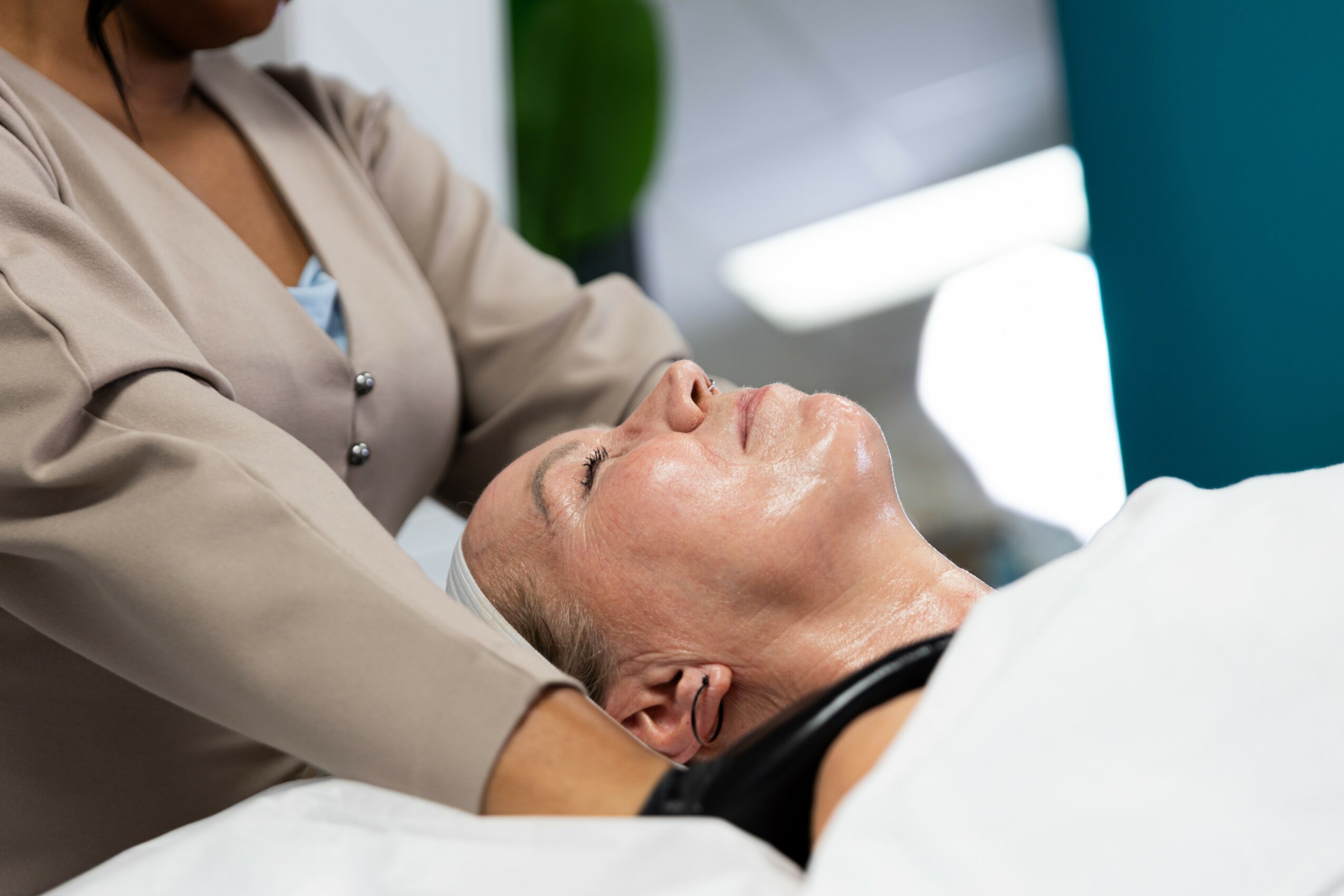 Person lying on a medical bed with eyes closed, receiving care from a healthcare professional.