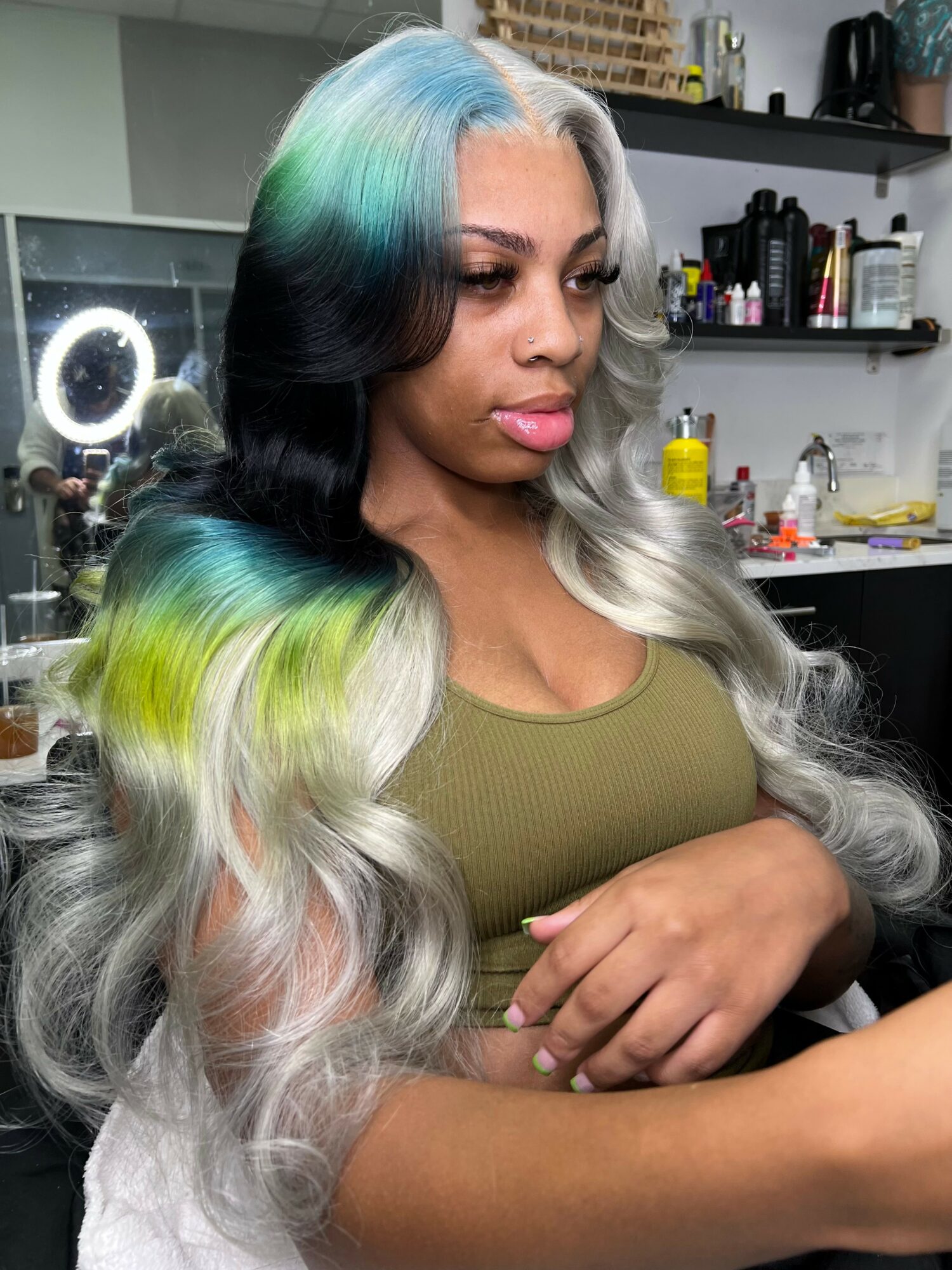 Woman with long, wavy hair dyed in shades of blue, green, black, and silver, in a salon setting.