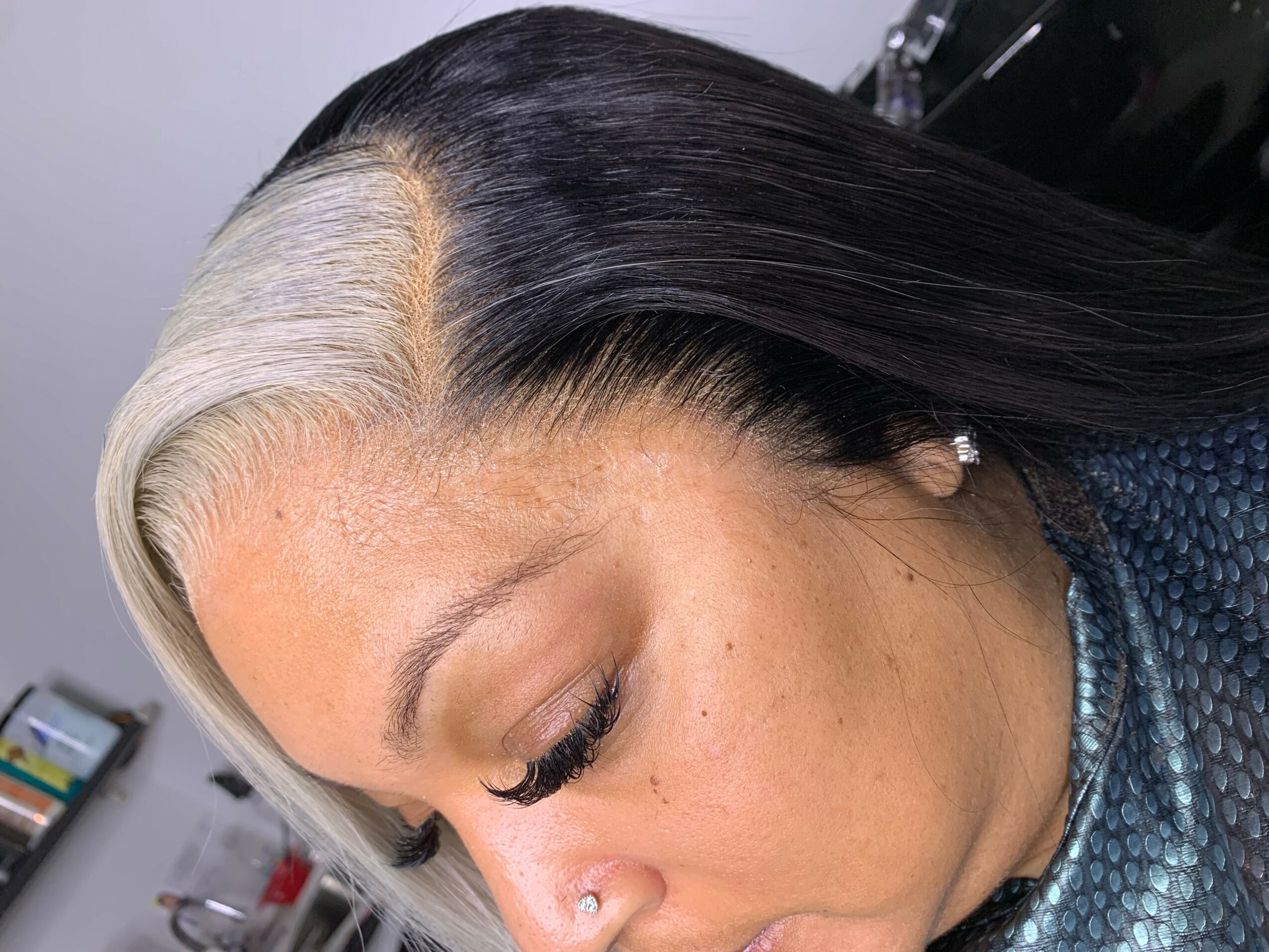 Side profile of a woman with black and white hair, closed eyes, and a nose piercing.