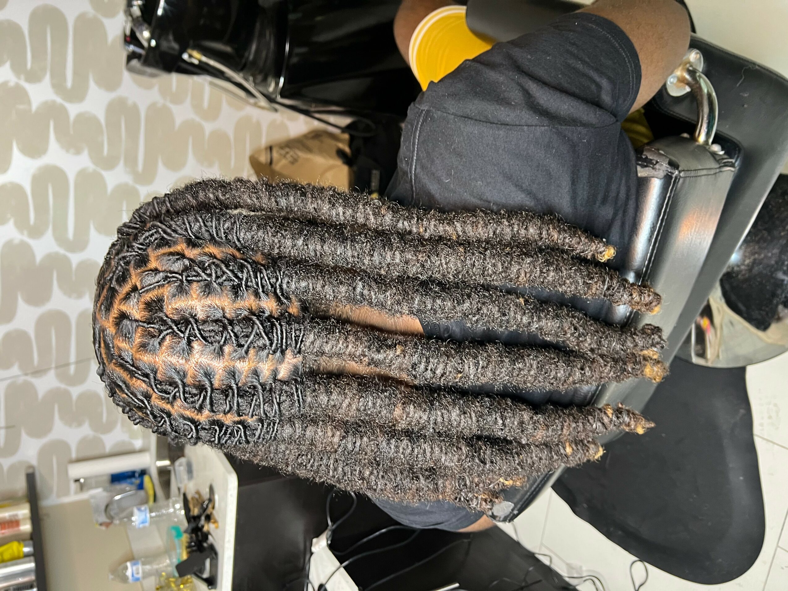 Person with long, textured braids sitting at a desk, viewed from above, with various objects on the desk.