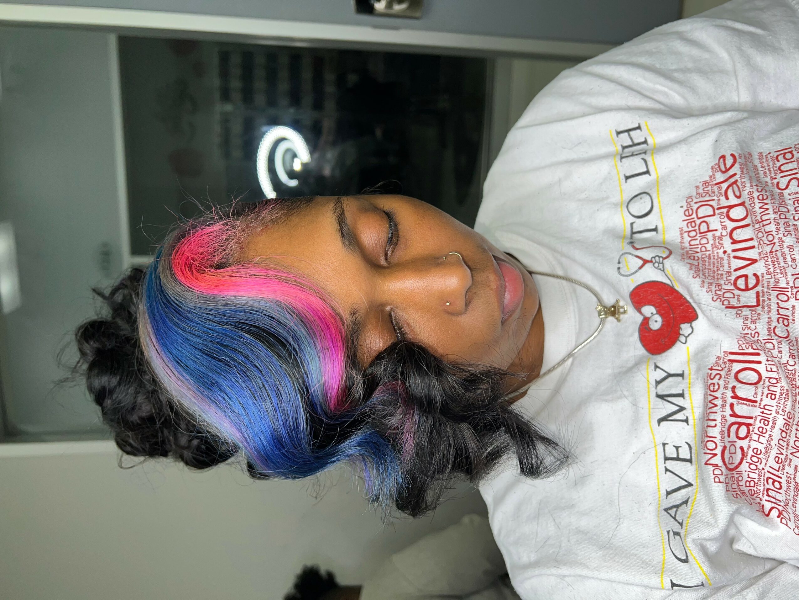 Woman with colorful hair styled in waves, wearing a white T-shirt with text and a red heart, sleeping or resting.
