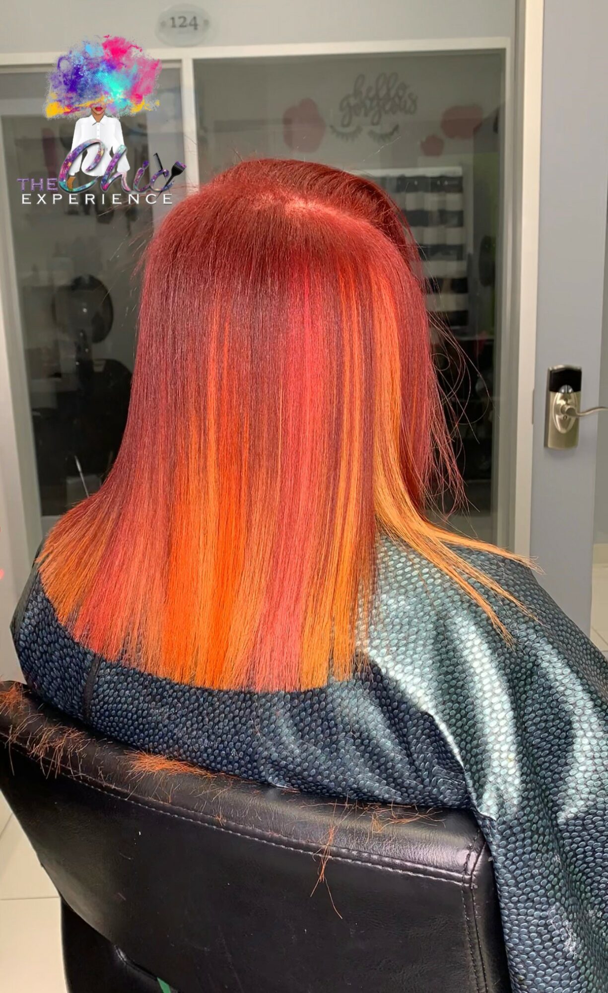 Person with straight, vibrant red and orange hair sitting in a salon chair, facing away from the camera.