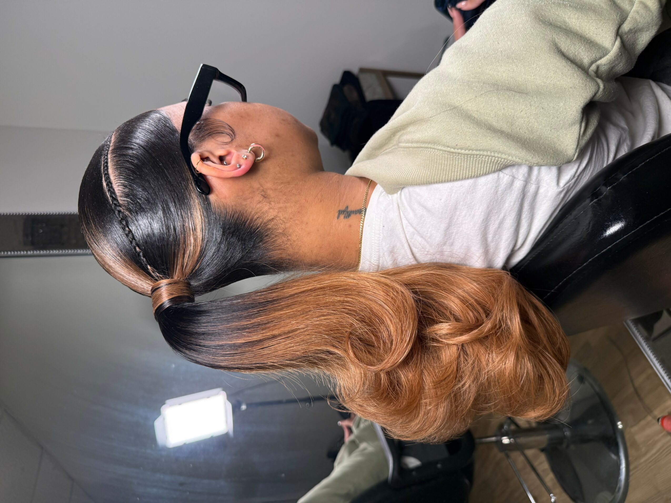 Person with long, wavy hair sitting in a chair, facing away, with a hairdresser working on their hair.
