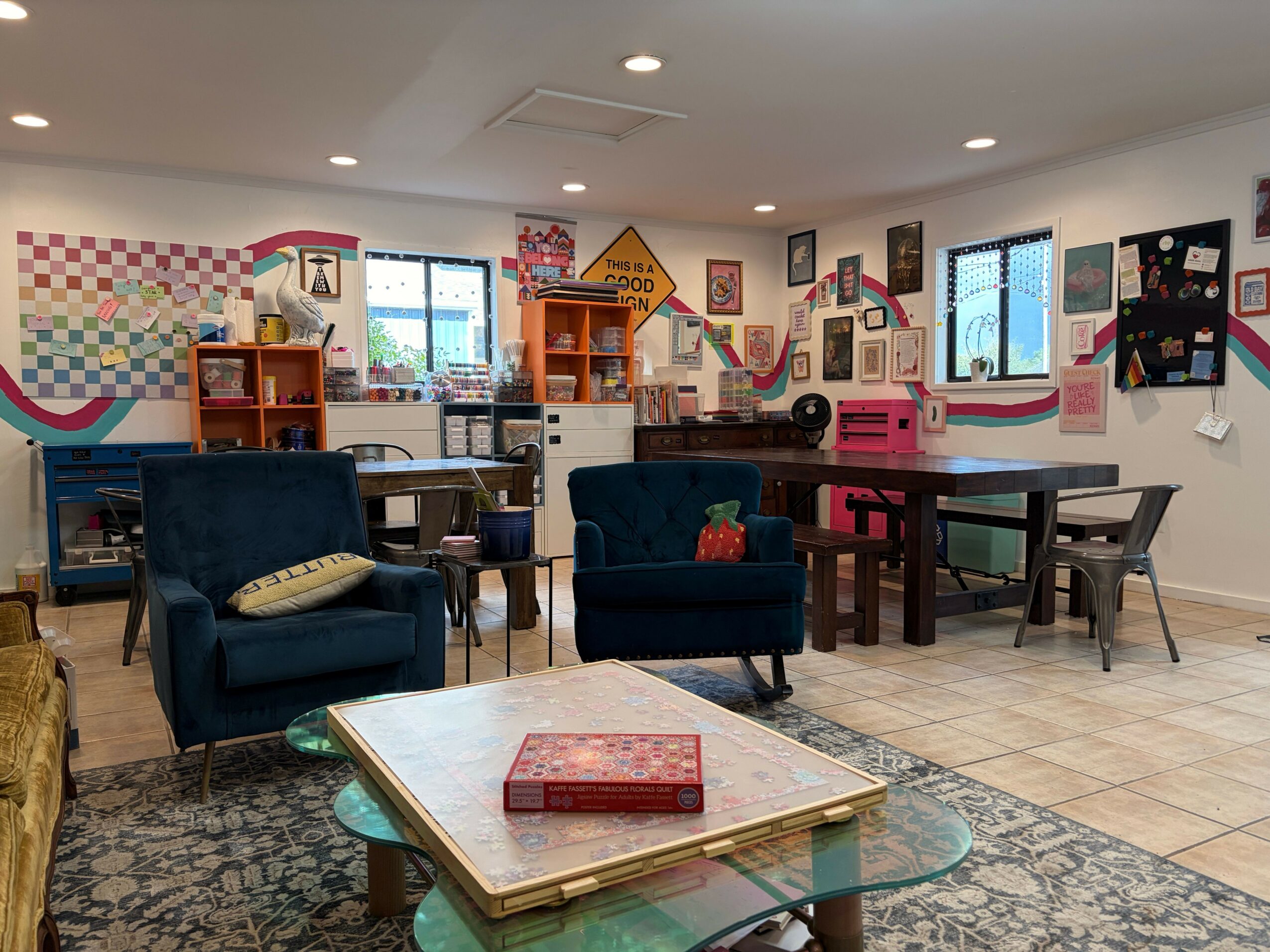 Living room with blue chairs, a glass table, and colorful wall decorations, seen from a rotated perspective.