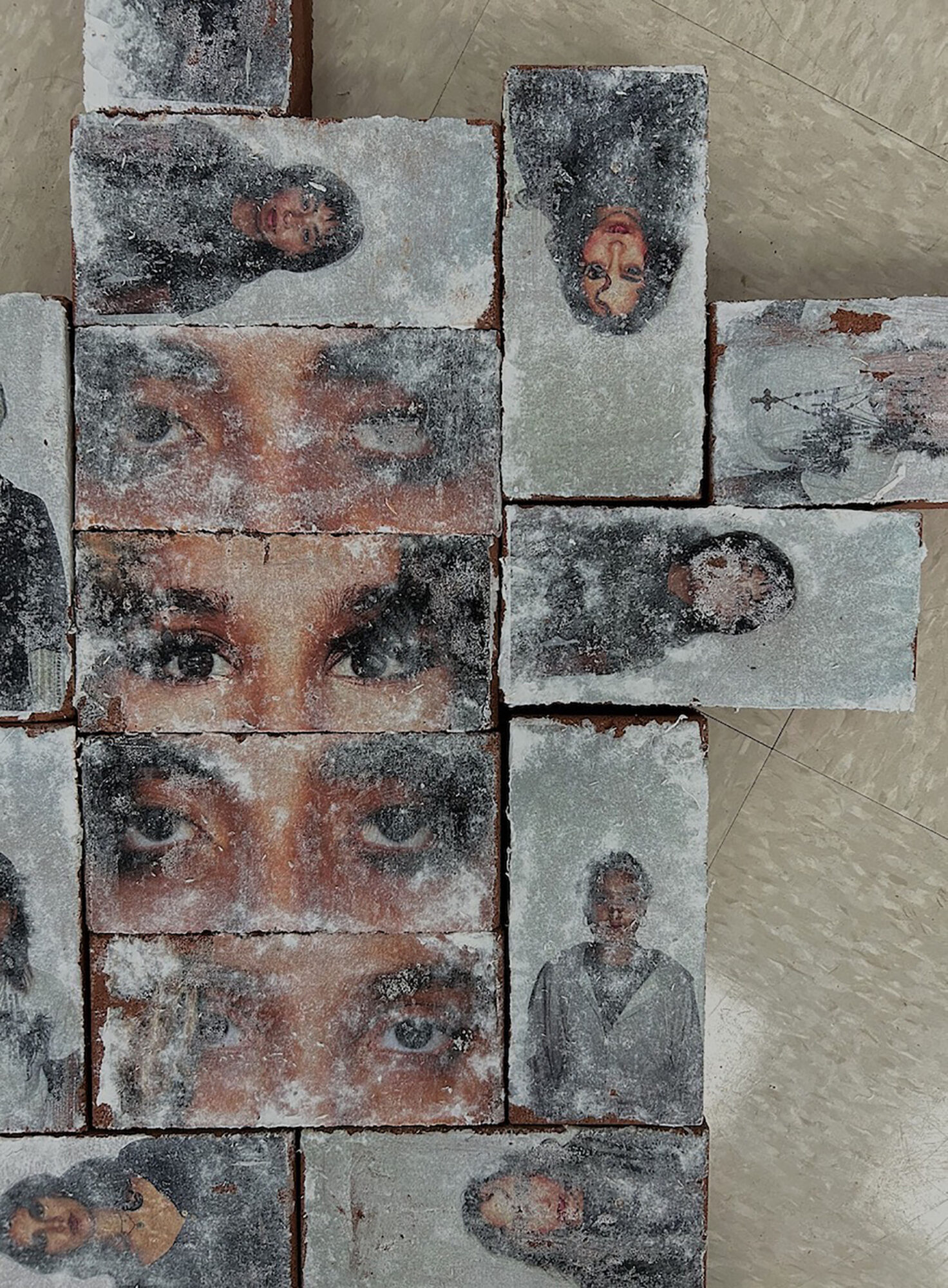 Multiple bricks with painted faces and a woman, arranged in a pattern, on a concrete surface.