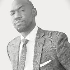 Man in suit and tie looking at camera, white background, black and white photo.