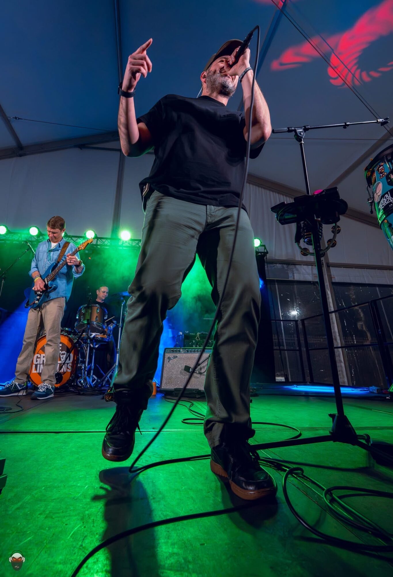 Performer singing into microphone on stage with band, green stage lights, and equipment visible.