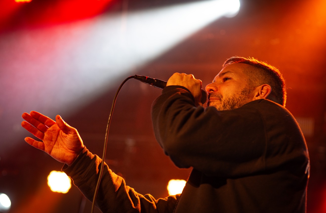Man singing into a microphone on stage with colorful lighting, eyes closed, expressive gesture, dark background