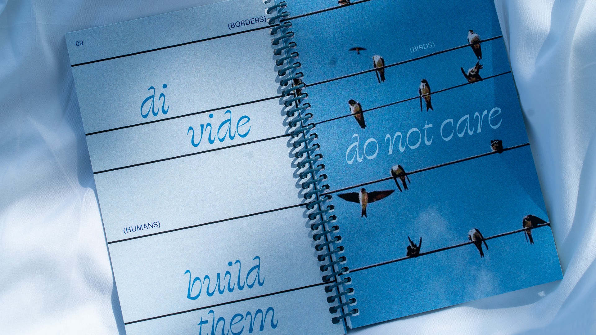 Open notebook with handwritten words and clothespins on lines, surrounded by white fabric, with blue background.