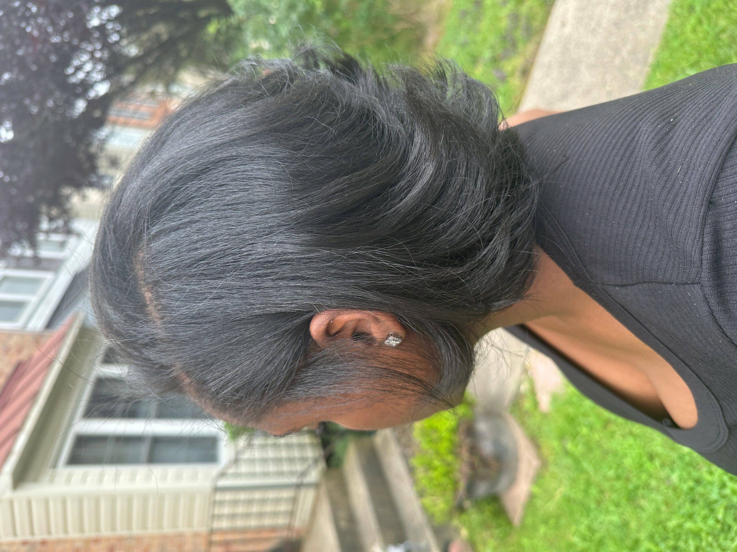 Side view of a woman with black hair, outdoors on a sidewalk, wearing a black top and blazer.
