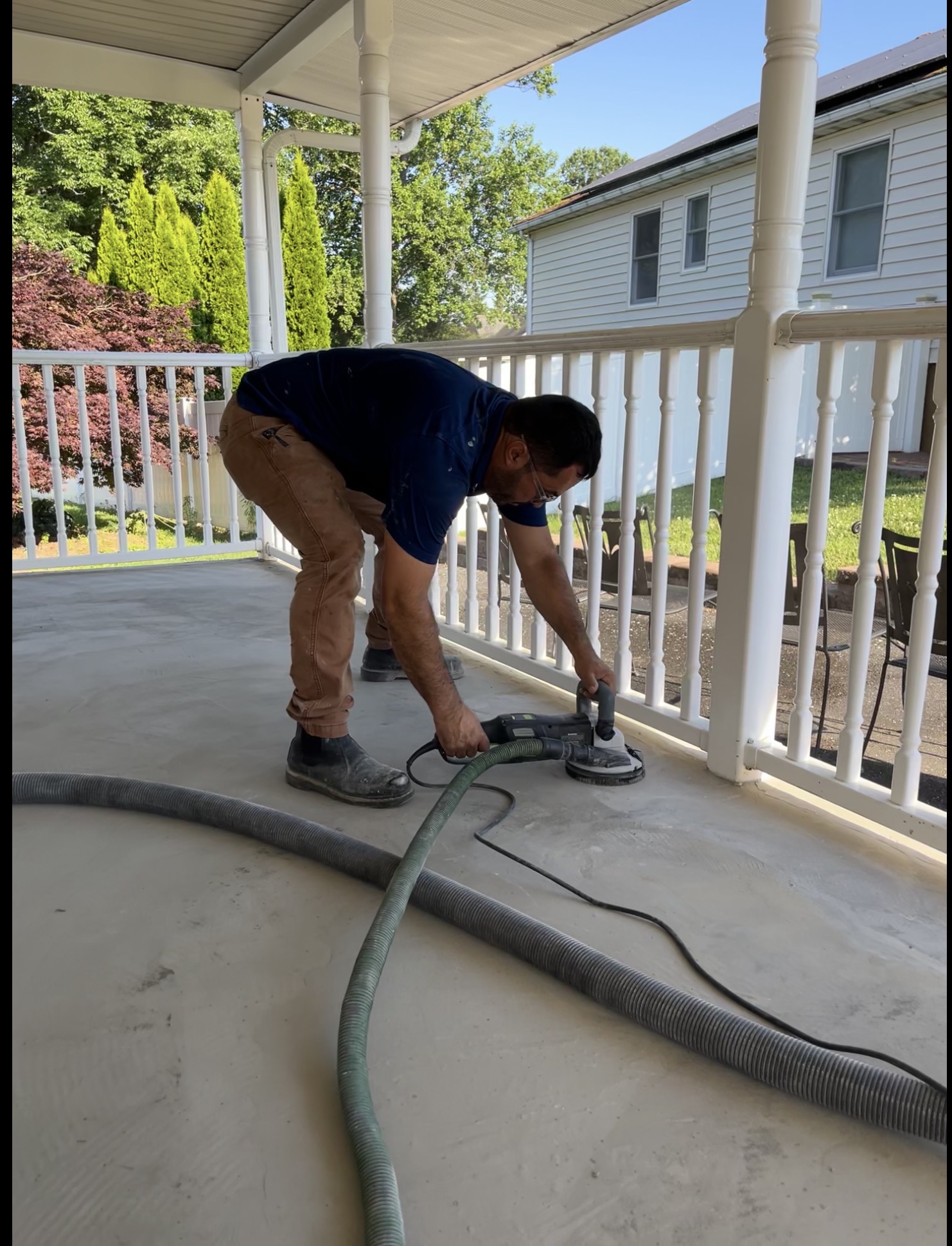 Person using a power sander on a porch floor, with a house and trees in the background.