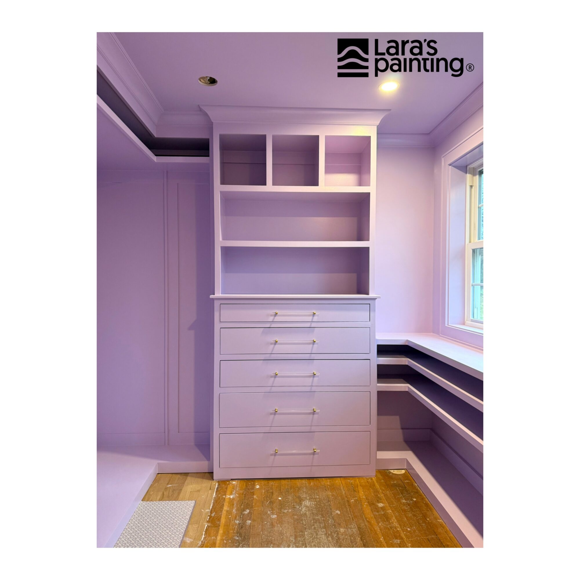 Purple room with built-in shelves and drawers, window on right, wooden floor, and ceiling light. Logo in top right corner.
