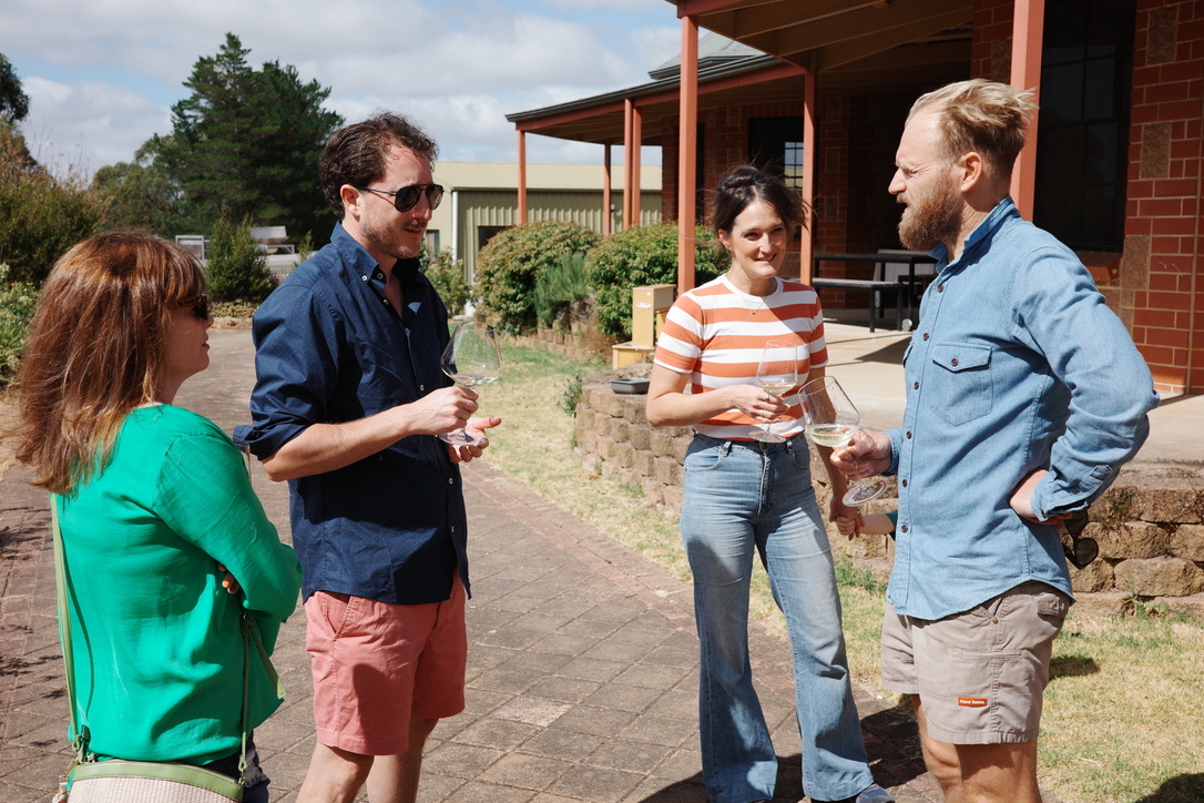Four people standing outdoors, talking and smiling, with a building and trees in the background.