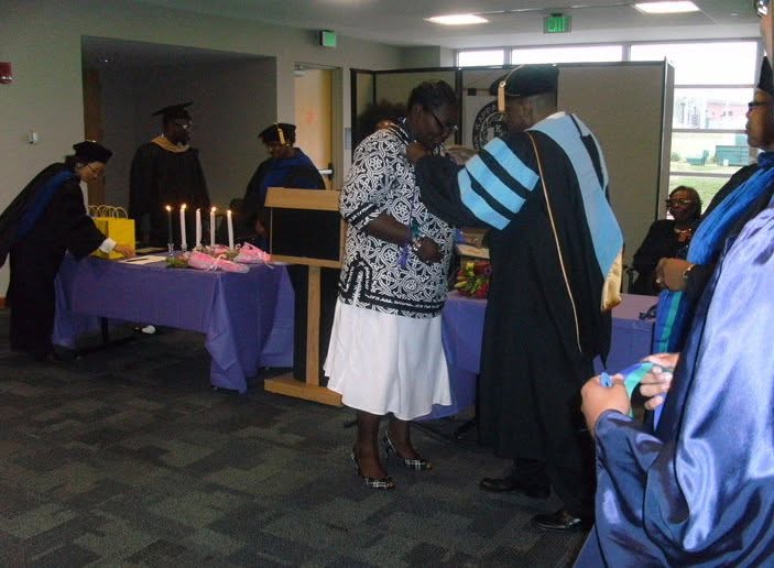 People at a graduation celebration with candles and decorations, some wearing caps and gowns, in an indoor setting.