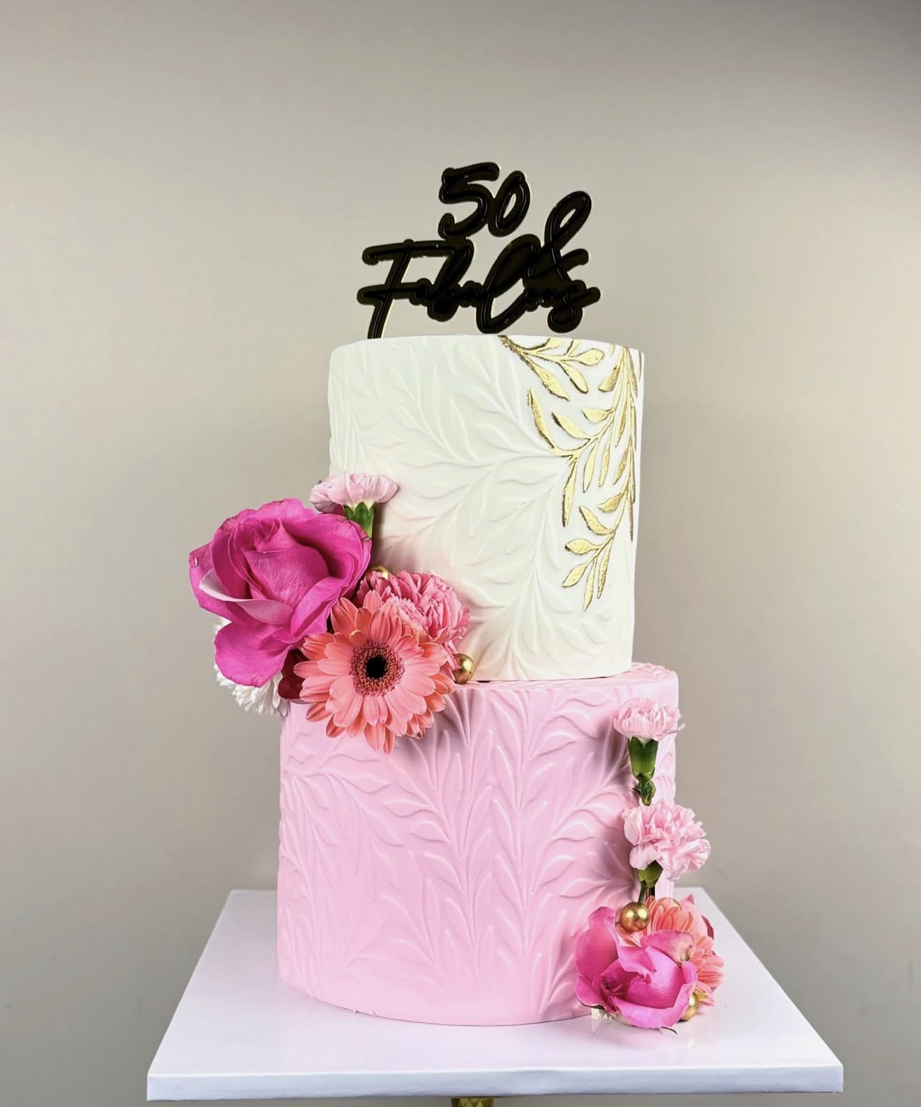 Two decorated cakes, one white and one pink, with flowers and a black topper that says '50 Fice'.