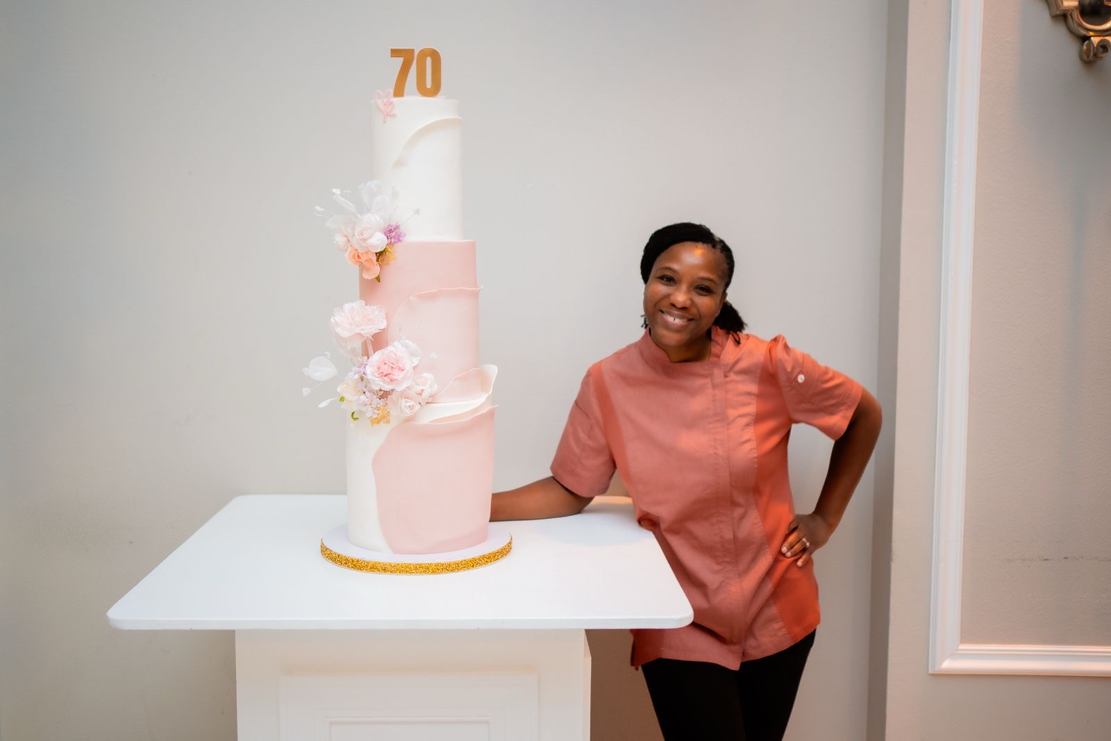 Young girl smiling next to a pink and white birthday cake with the number 70 on top, on a white table.