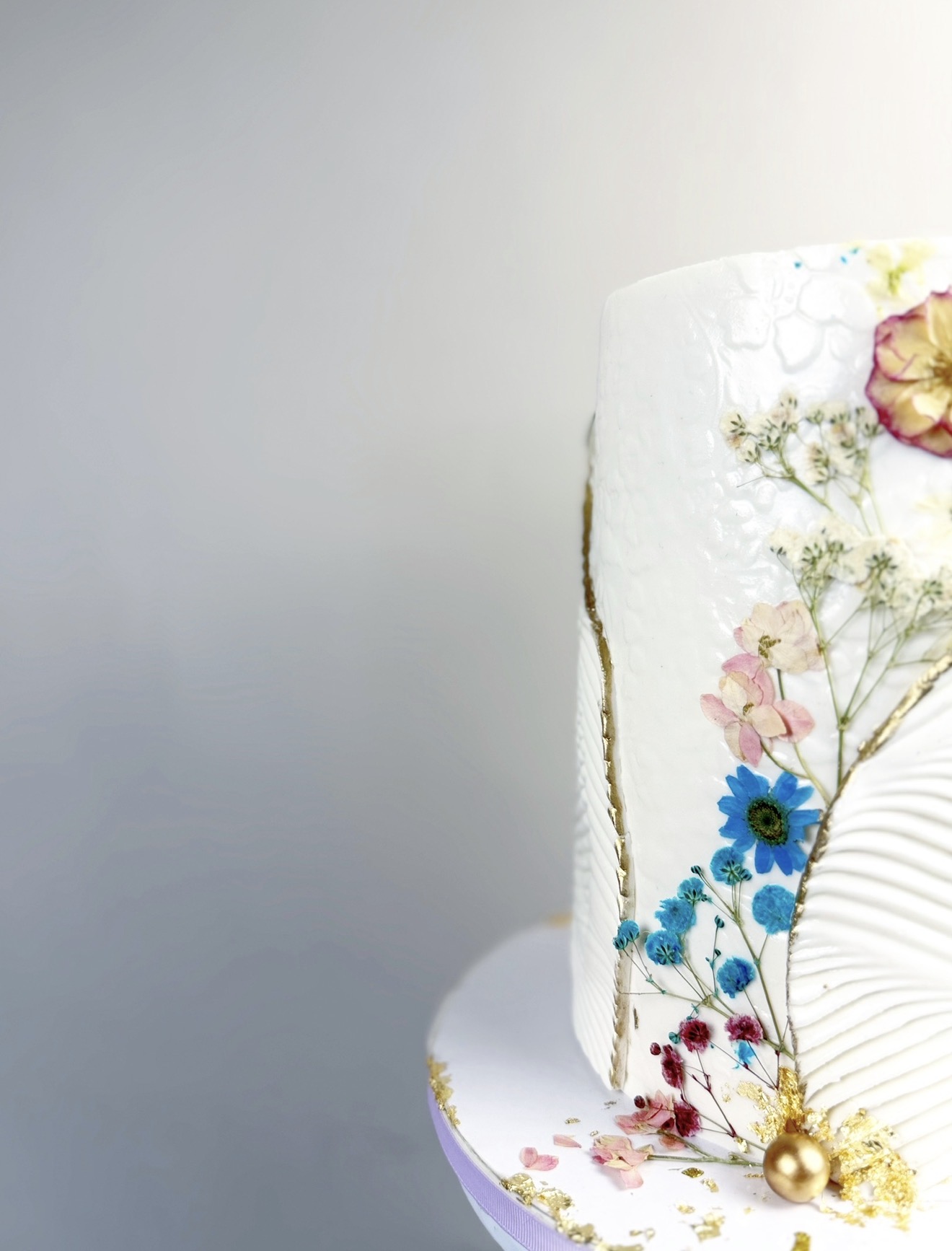 Close-up of a decorated cake with floral designs and gold accents, against a plain background.