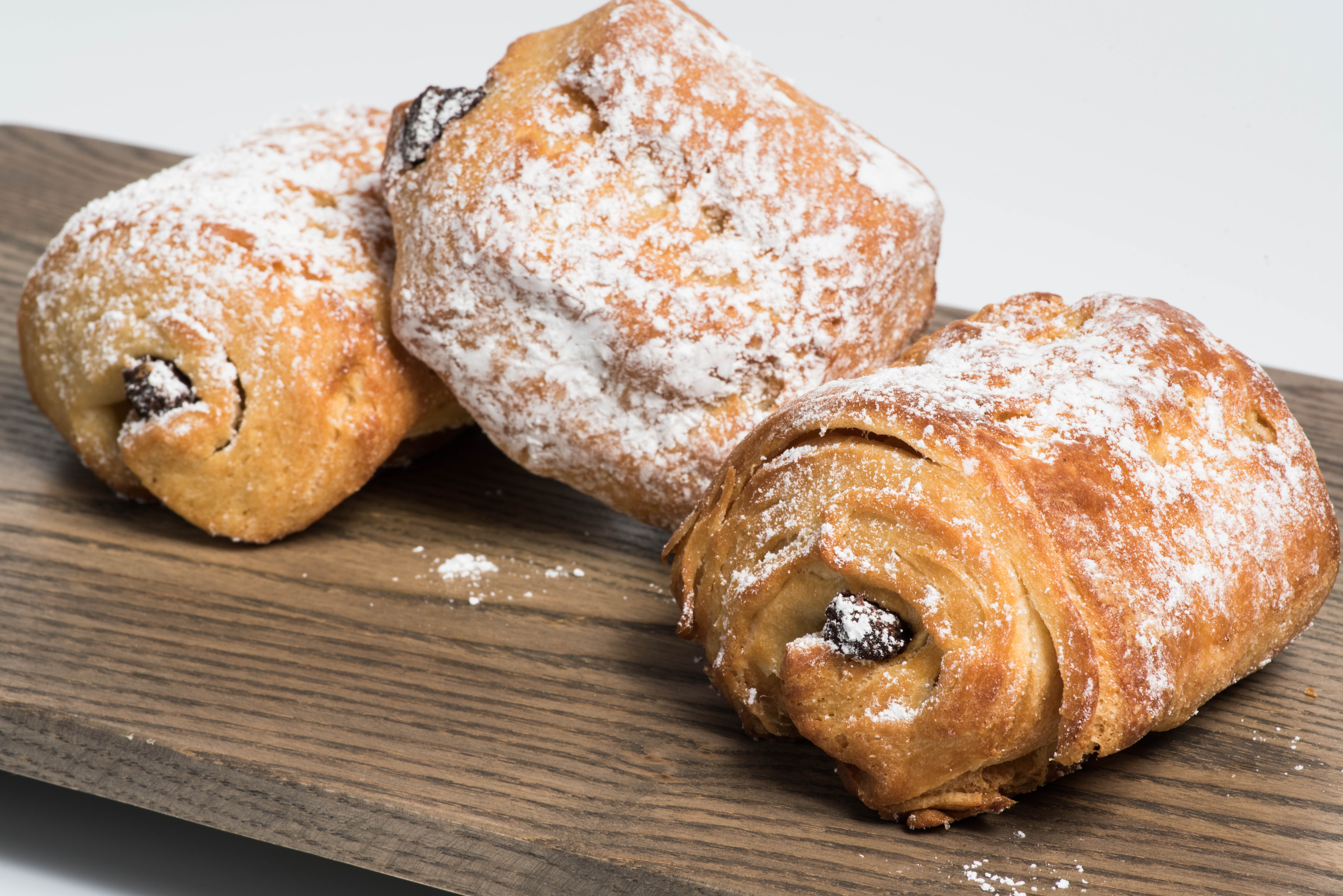 Three powdered sugar-dusted pastries with dark filling on a wooden surface.