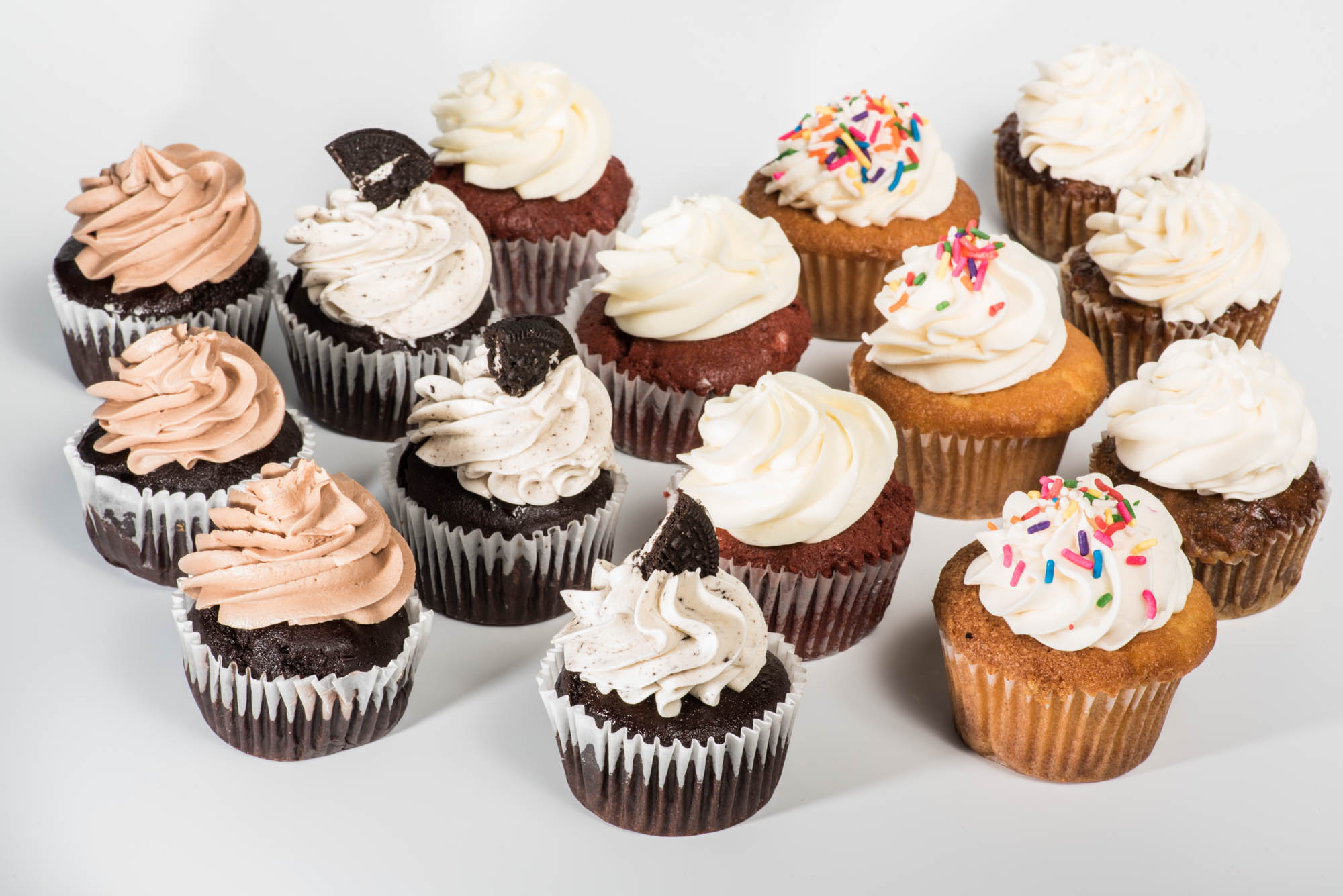 Assorted cupcakes with frosting and sprinkles on a white background.