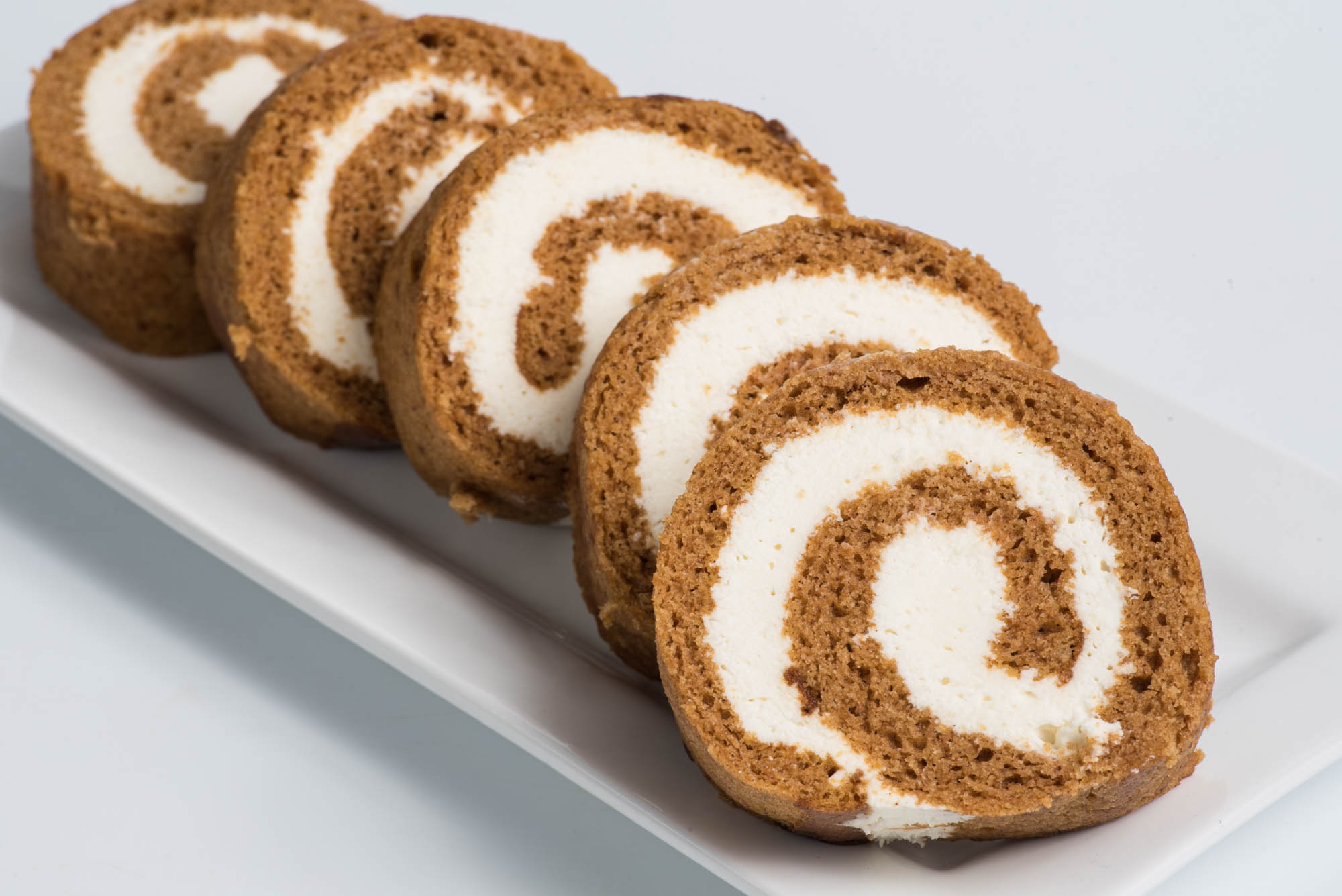 Four slices of a rolled cake with white filling on a white rectangular plate.