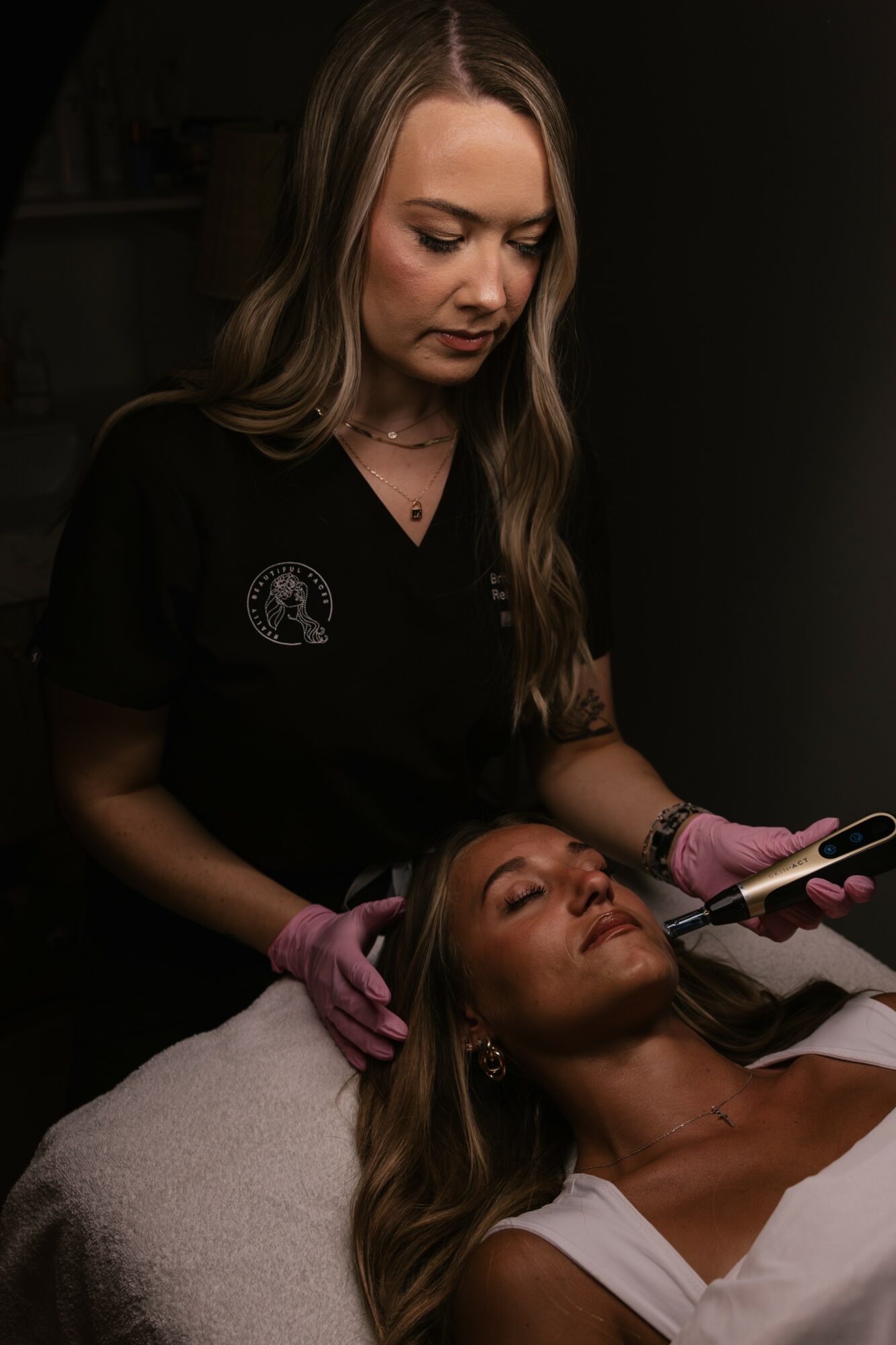A woman receives a cosmetic treatment from a professional in a dark room.