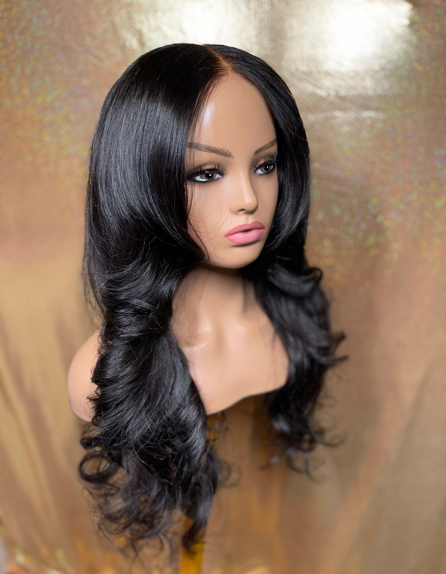 Bust of a woman with long, wavy black hair and makeup, against a gold background.