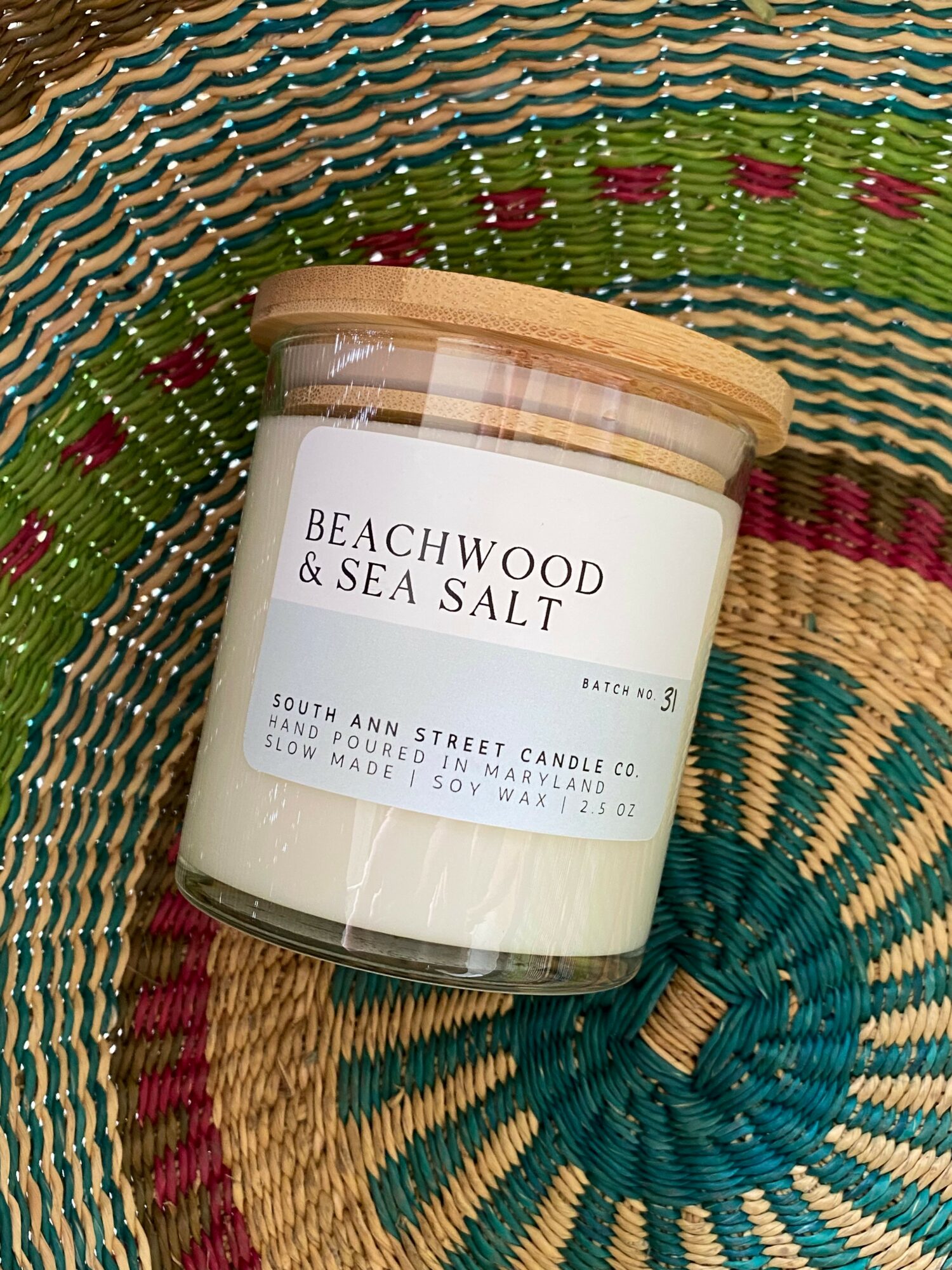 A candle jar labeled 'Beachwood & Sea Salt' on a colorful woven surface.