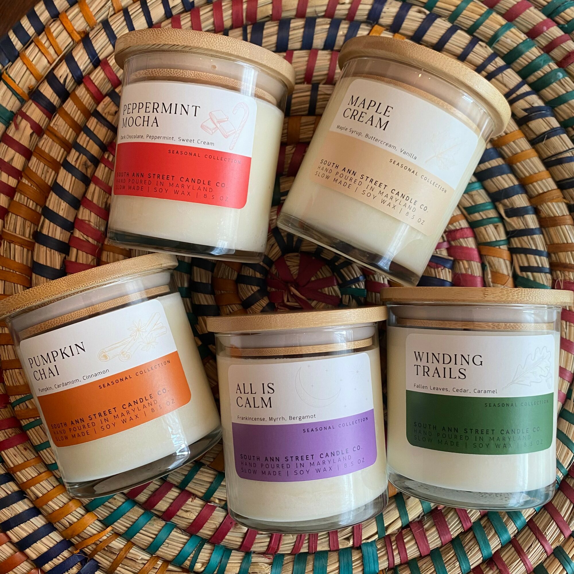 Five candles in a woven basket, each with different labels and colors, arranged in a circle.