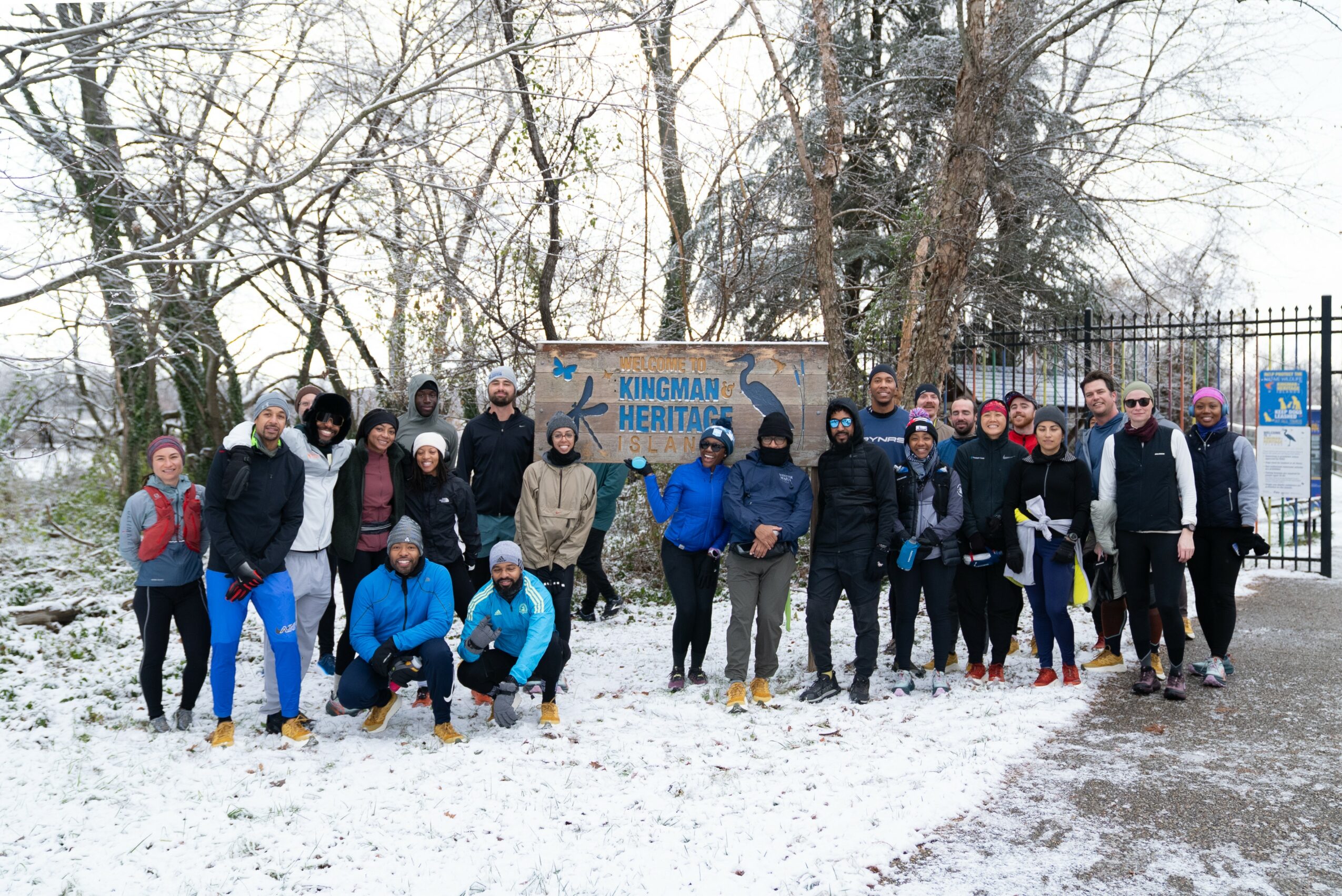 Group of people standing outdoors on snow-covered ground near a sign that reads 'Kincard Heritage,' with trees and a fence in the background.