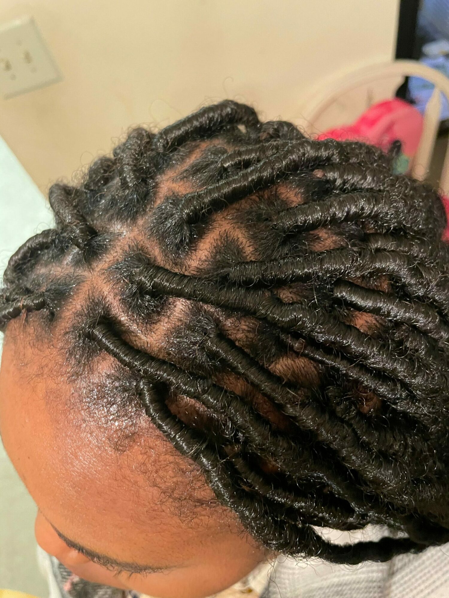 Top view of a person with styled dreadlocks, showing the hair pattern and scalp, with a blurred background.