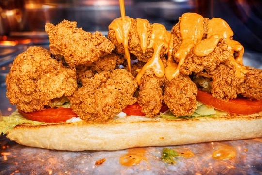 Fried chicken pieces with sauce on a sandwich bun, with vegetables underneath, on a plate.