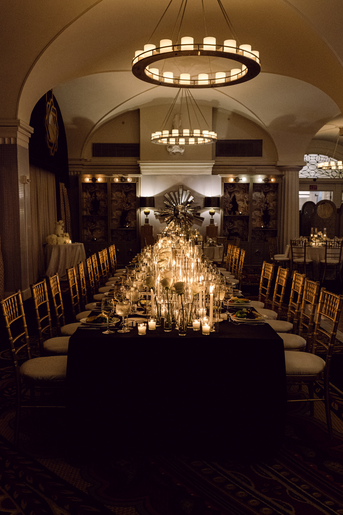 Elegant dining room with a long table, chandeliers, and warm lighting, set for a formal event.