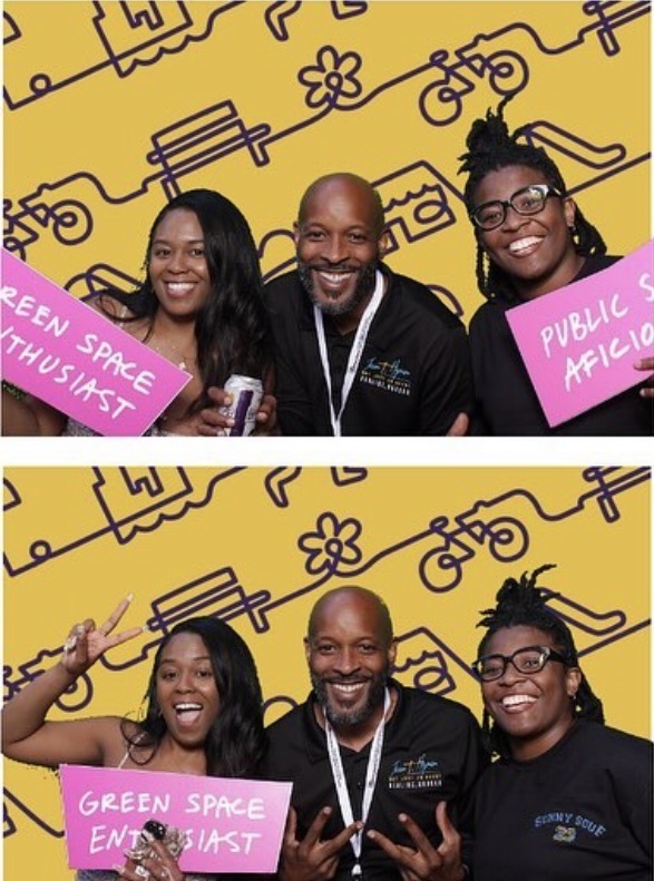 Three people smiling, two women and one man, holding signs and making peace signs, with a yellow background and black line drawings.