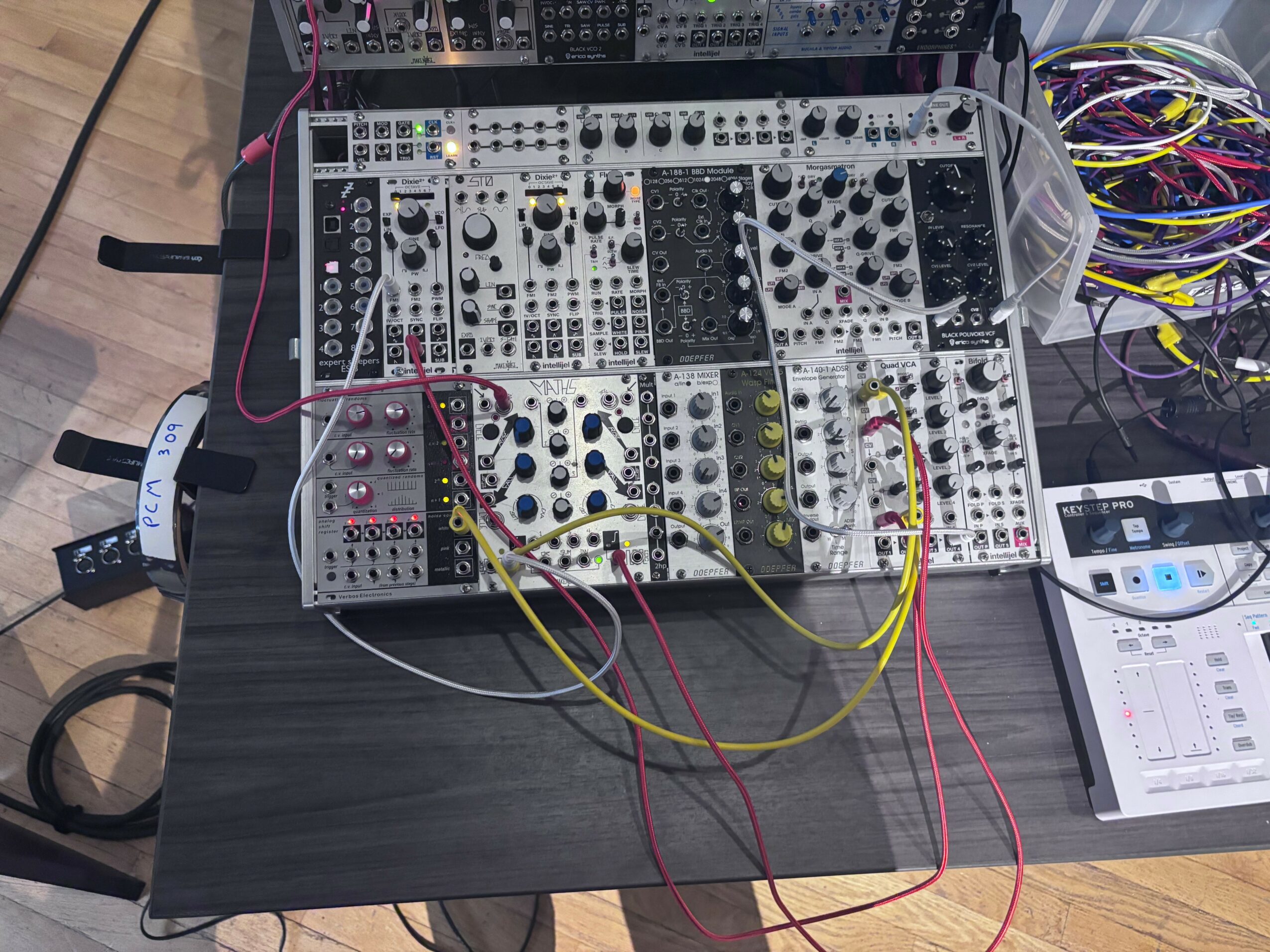 Electronic music equipment with knobs, cables, and a digital device on a black table.