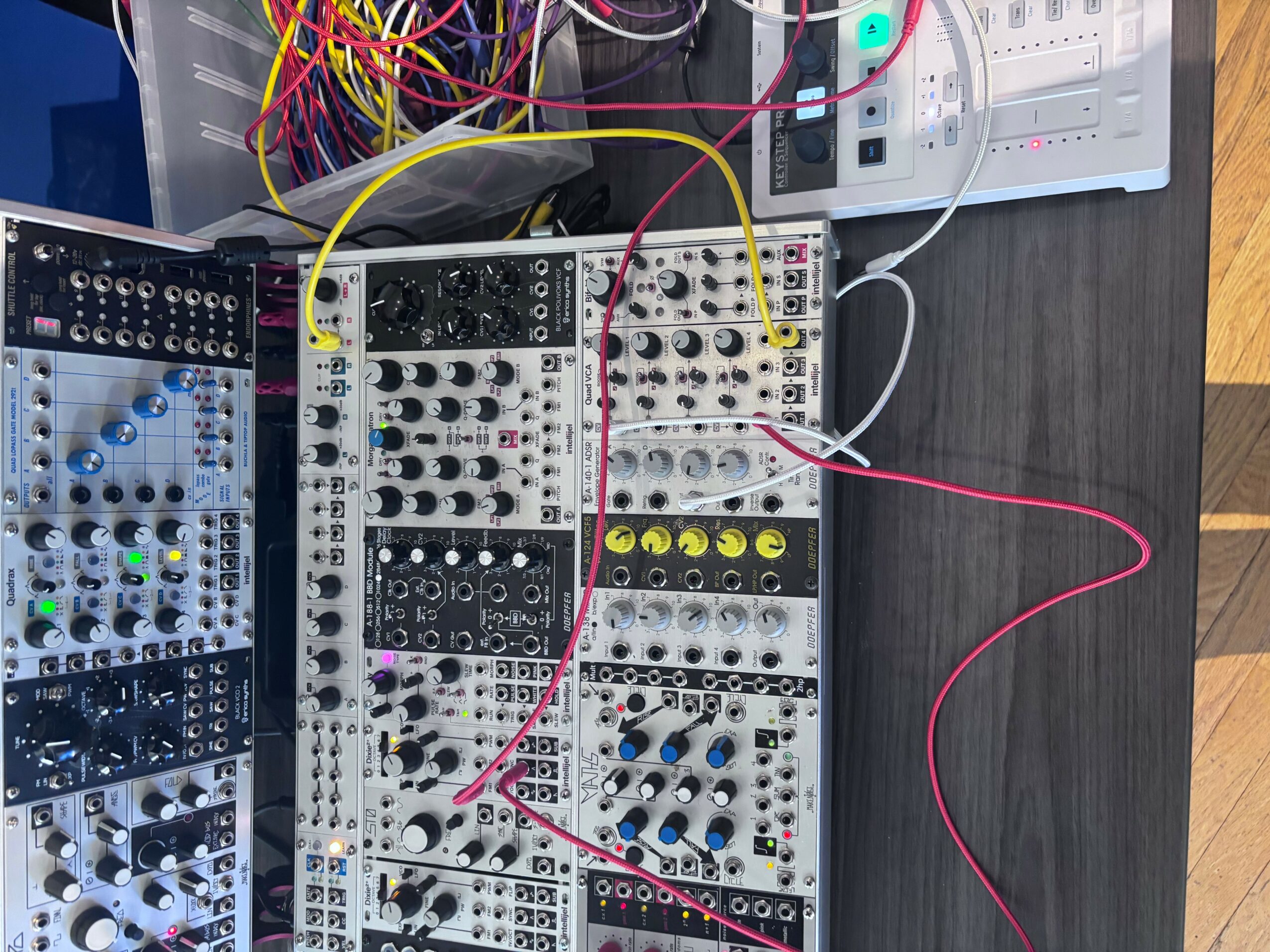Electronic synthesizer modules with colorful cables on a dark table, viewed from the side. Word count: 20.