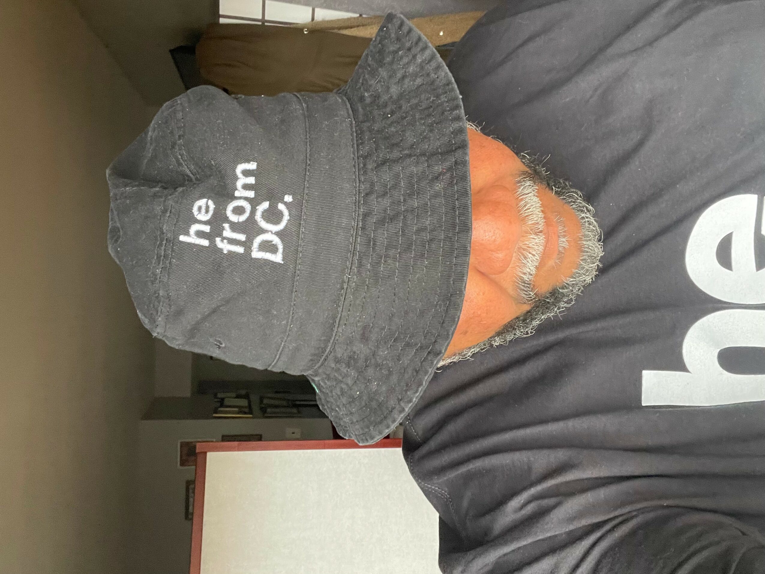 Person wearing a bucket hat with text, partially visible face, and a dark shirt, indoors.