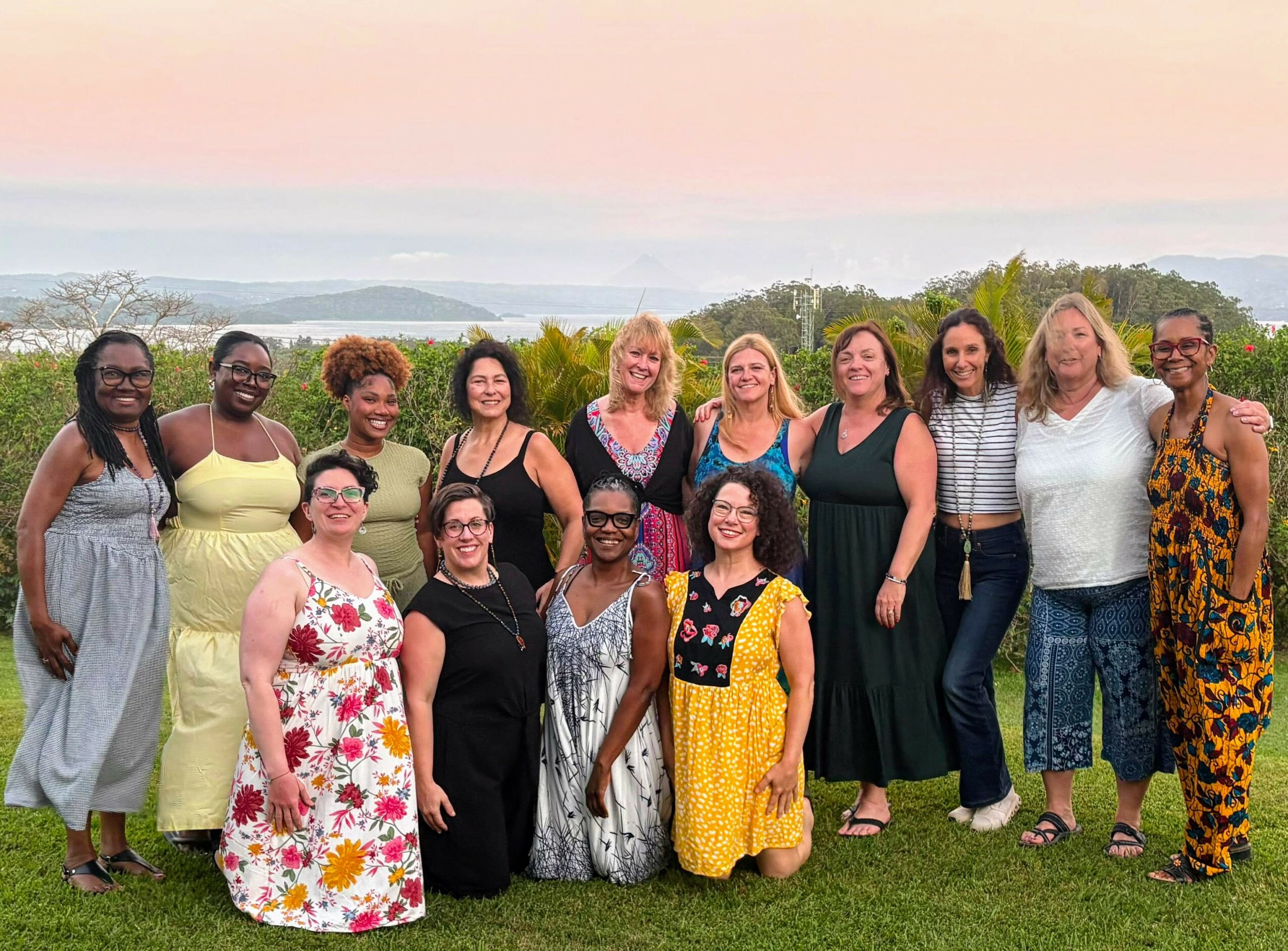 Group of women standing outdoors on grass with a scenic landscape and sky in the background.
