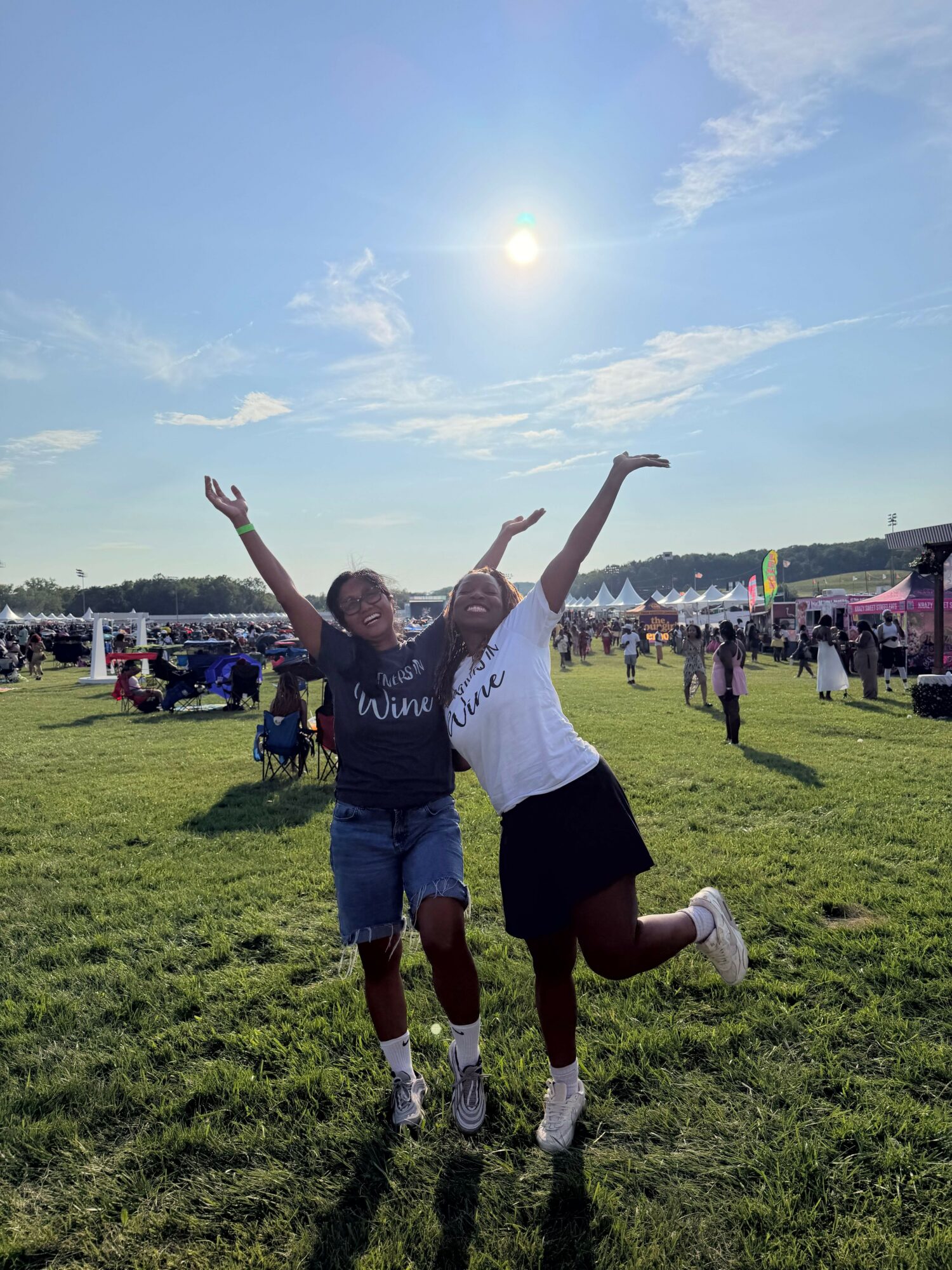 Two people standing on grass with arms raised, sunny sky, and cityscape in the background.
