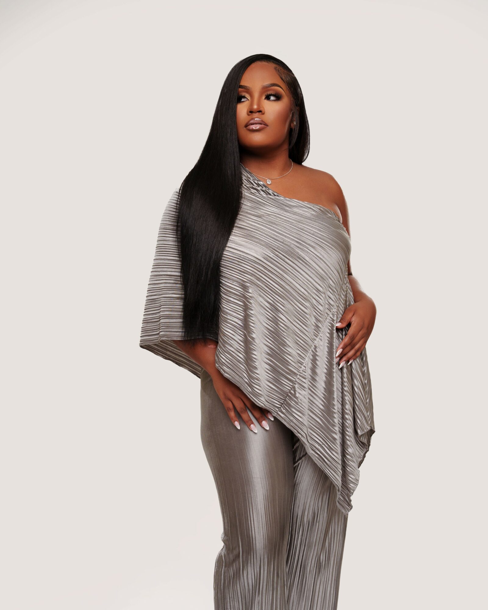 Woman with long black hair wearing a gray striped off-shoulder top and matching pants, standing against a plain background.