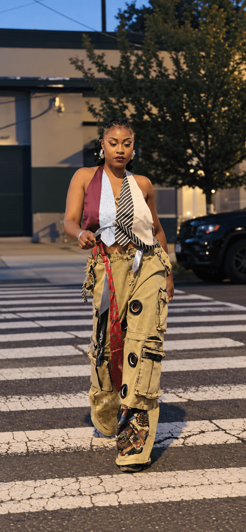 Young woman walking across a crosswalk in an urban area, wearing colorful pants and a sleeveless top.