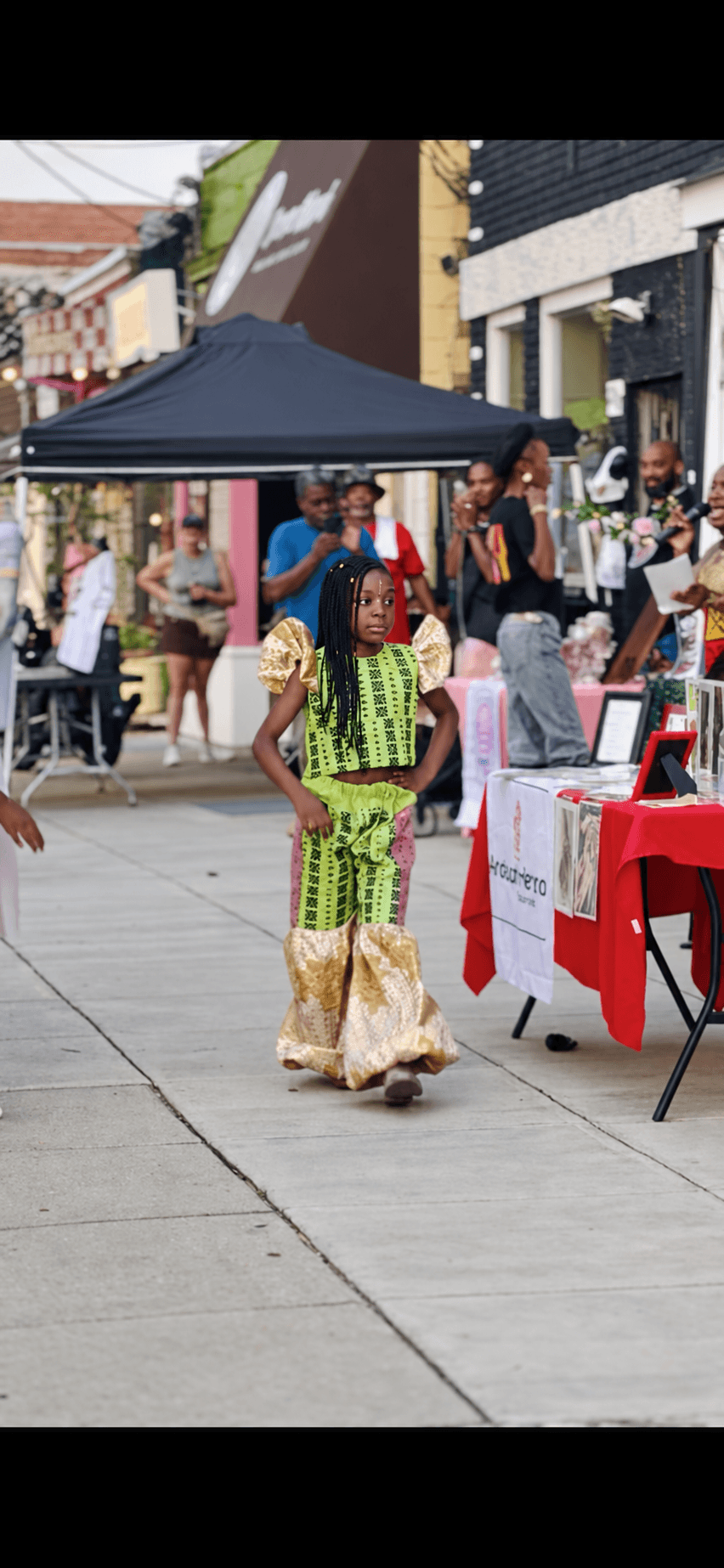 Person in colorful traditional attire walking on a busy outdoor street with tables and people in the background.