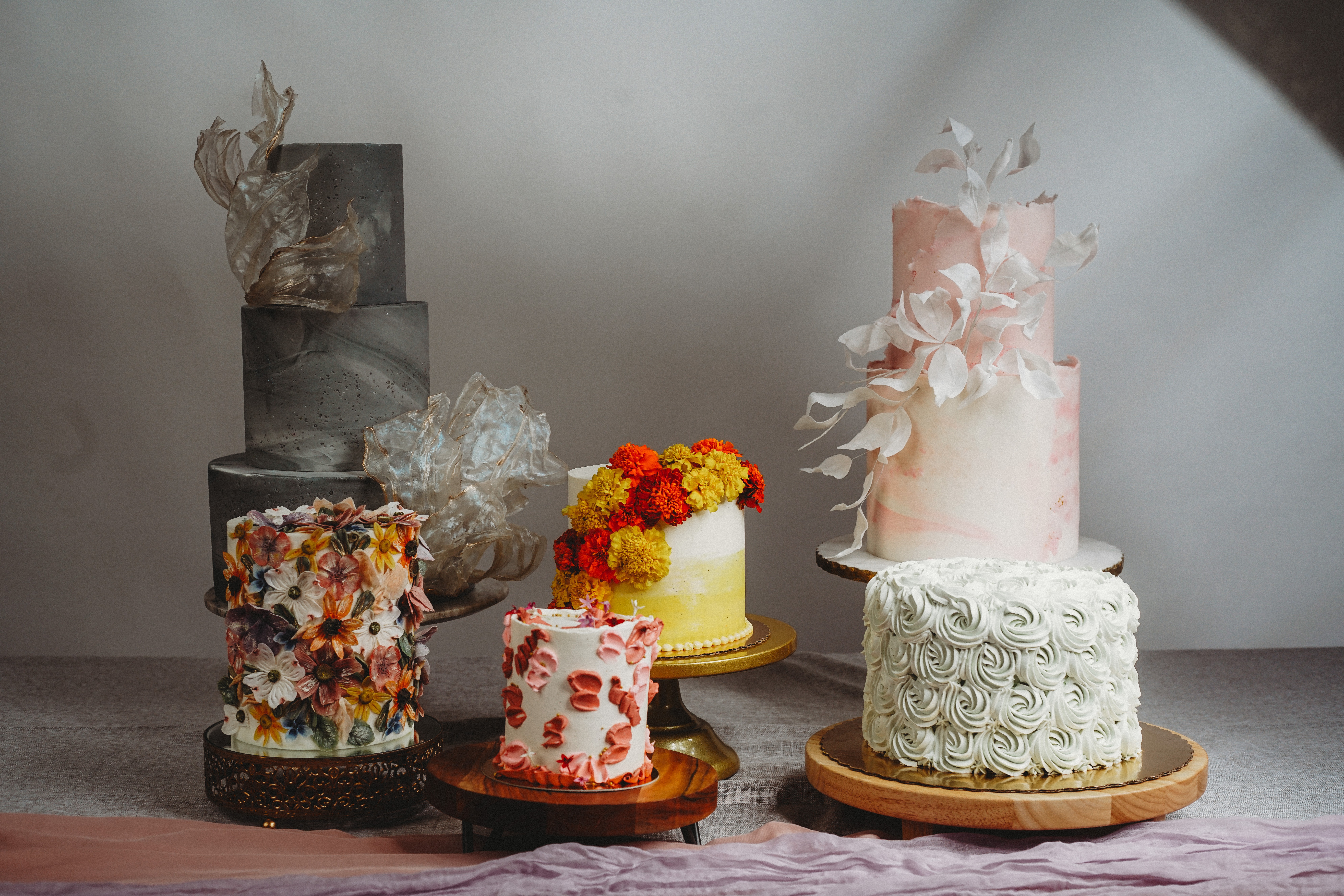 Six decorated cakes on a table with a plain background, featuring various colors and textures.