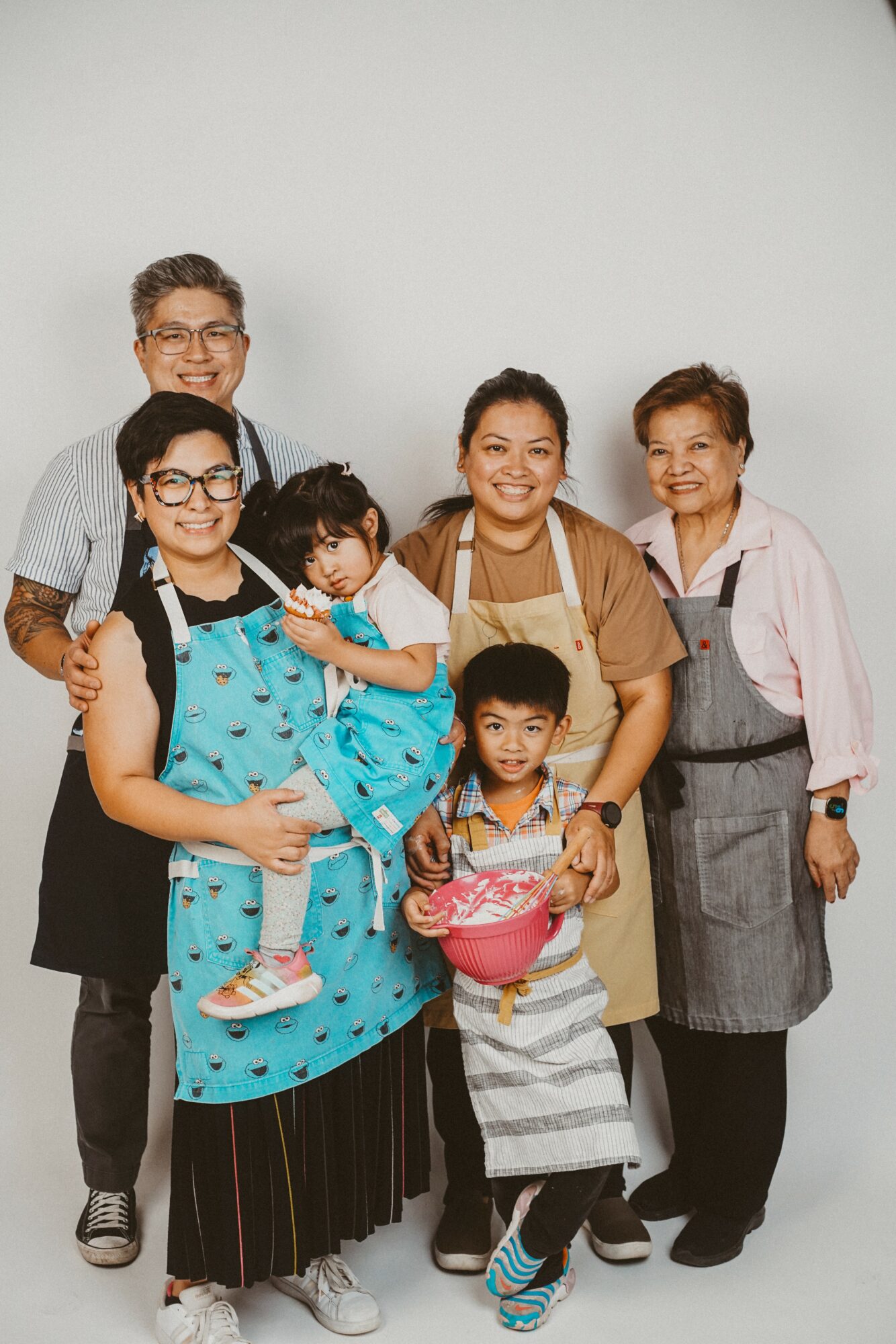 Group of six people, including children and adults, standing together against a plain background, smiling at the camera.