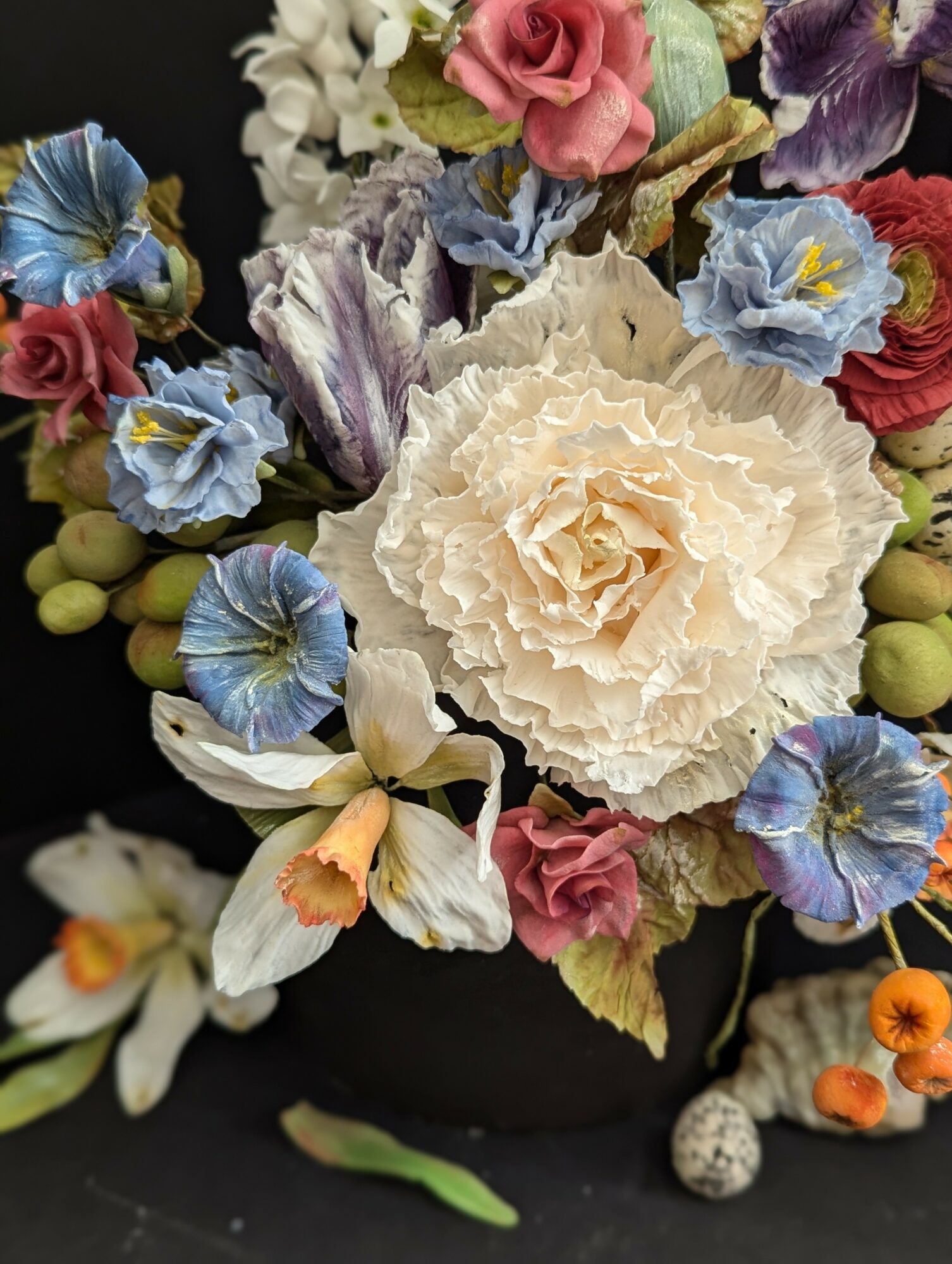 Arrangement of various colorful flowers including white, pink, purple, and blue blooms in a black vase.