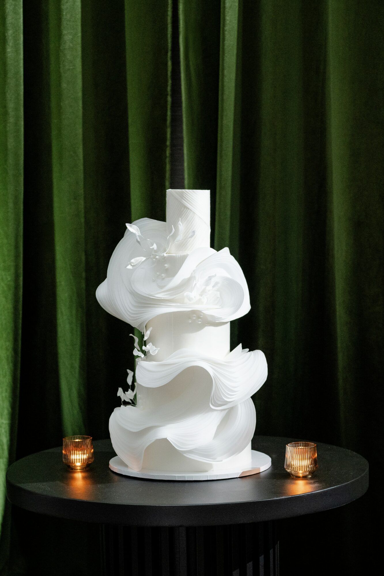 White abstract sculpture on black table with green curtain background, two small candles on sides, 20 words.