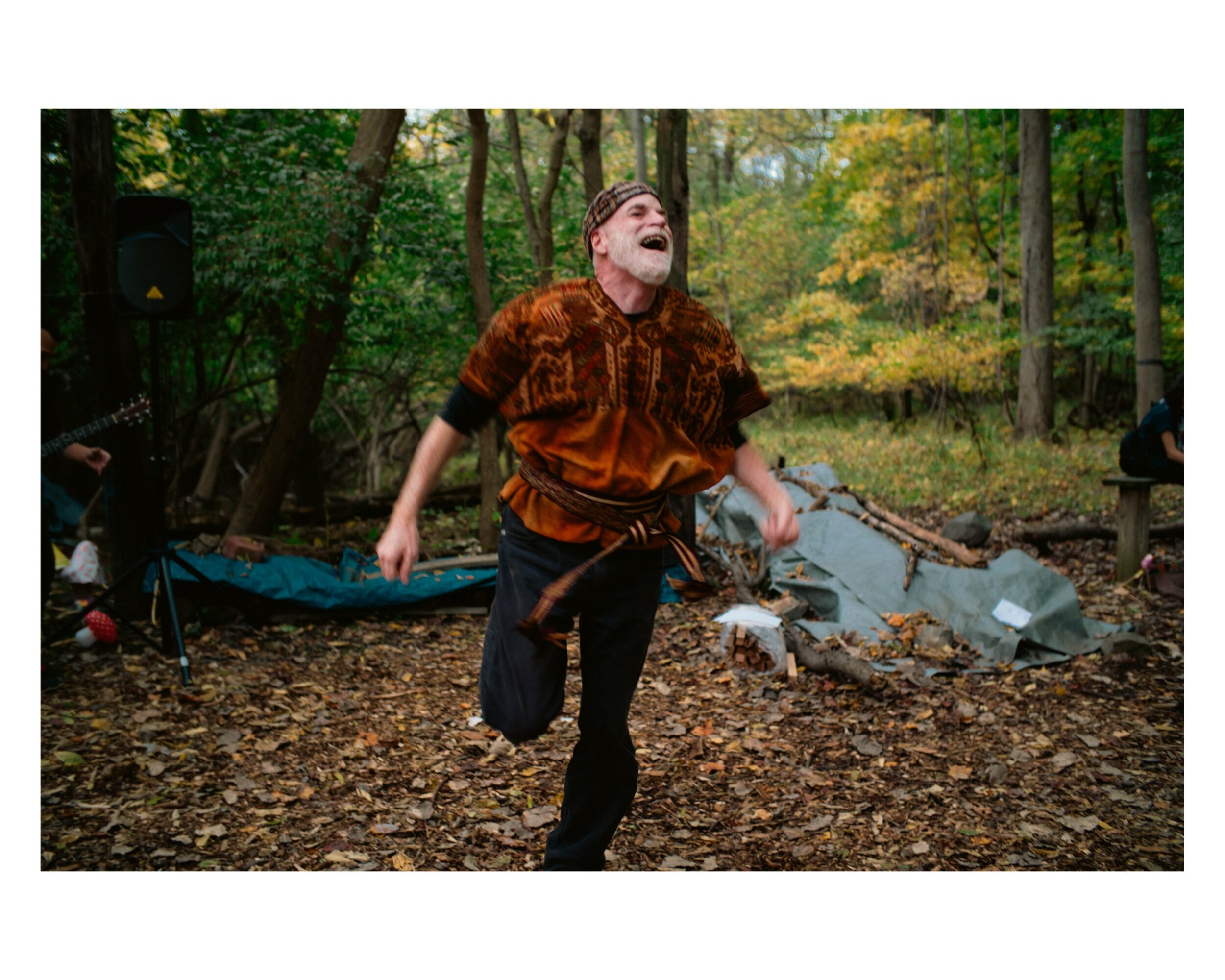 Person laughing and running outdoors in a wooded area with fallen leaves and rocks.