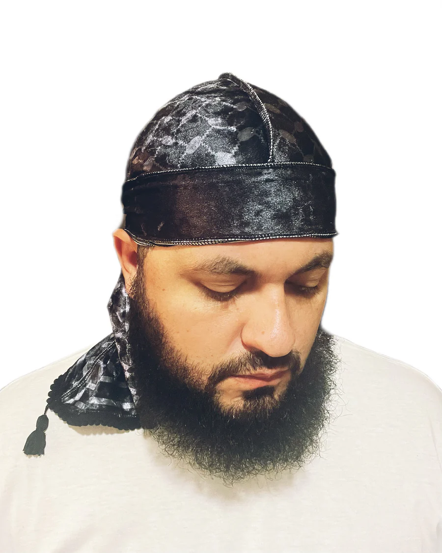 Man with a beard wearing a black durag, looking downward, against a white background.