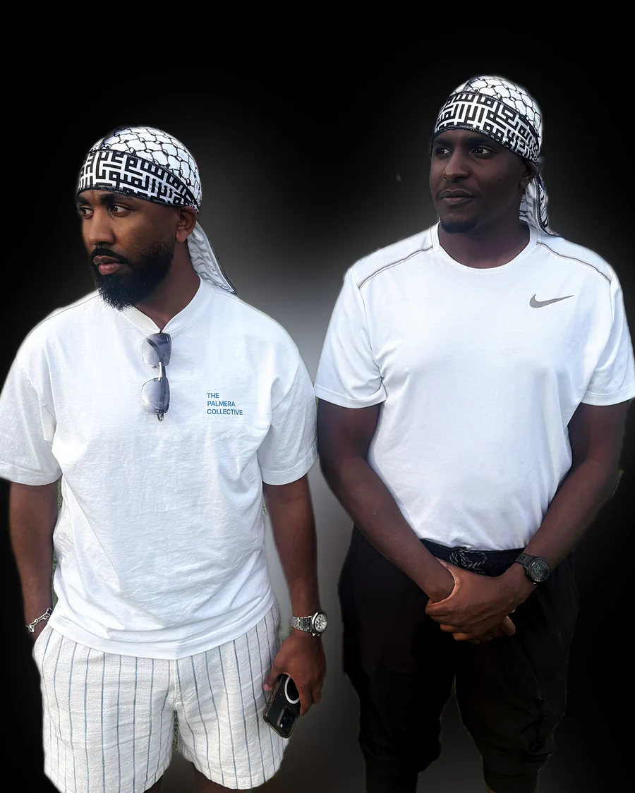 Two men stand side by side wearing white shirts and patterned headscarves, against a black background.